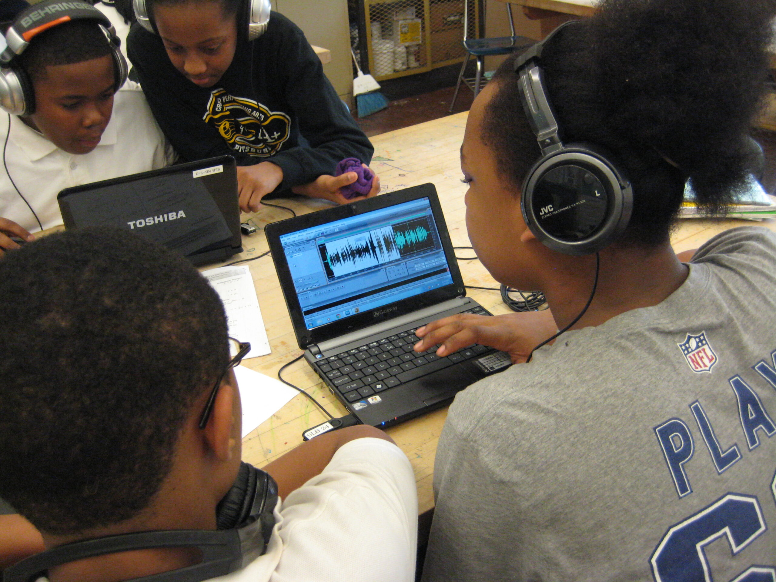 Four youth wearing headphones looking at audio editing software on laptop computers