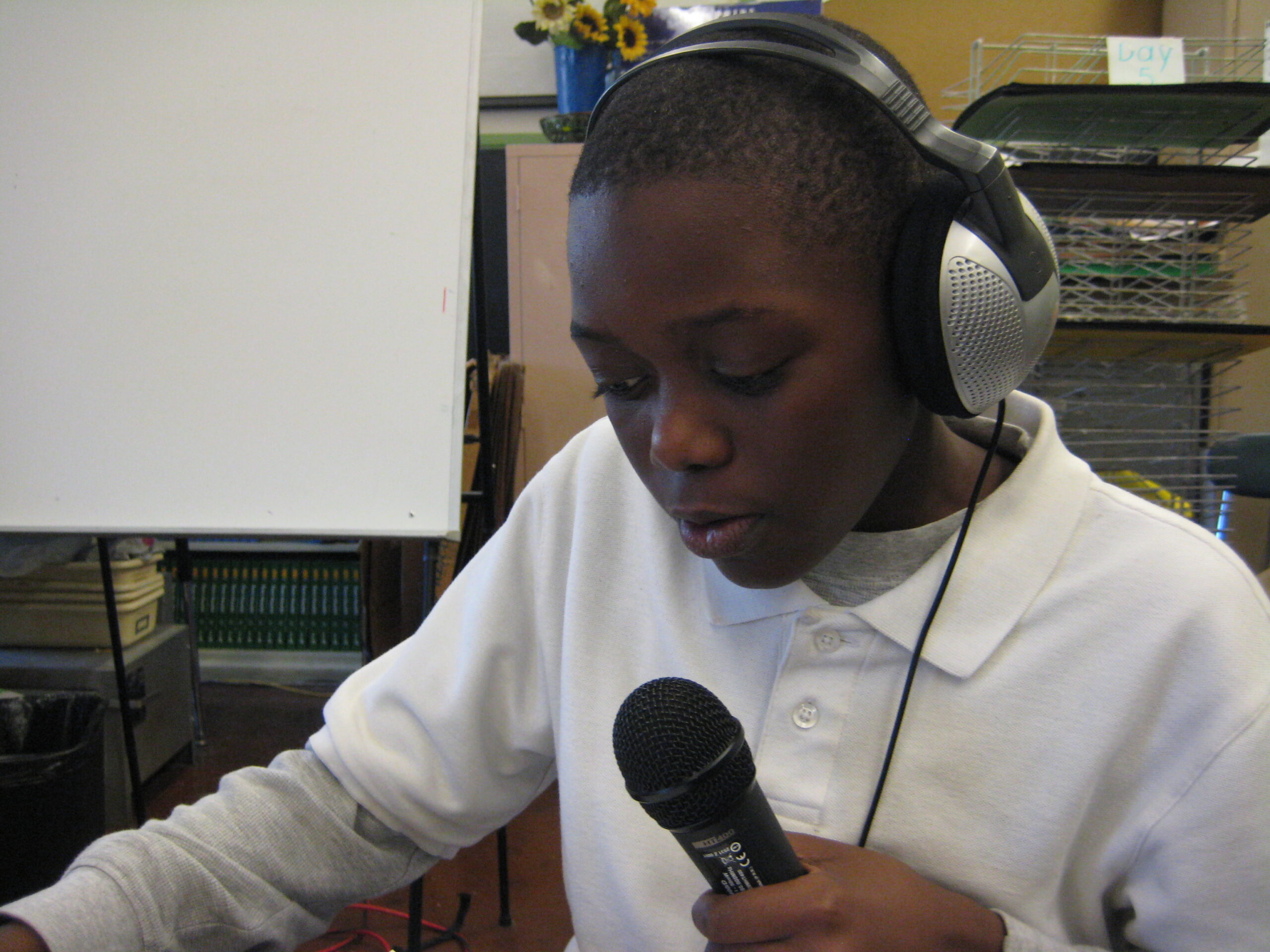A youth wearing headphones speaking into a microphone while sitting in a classroom