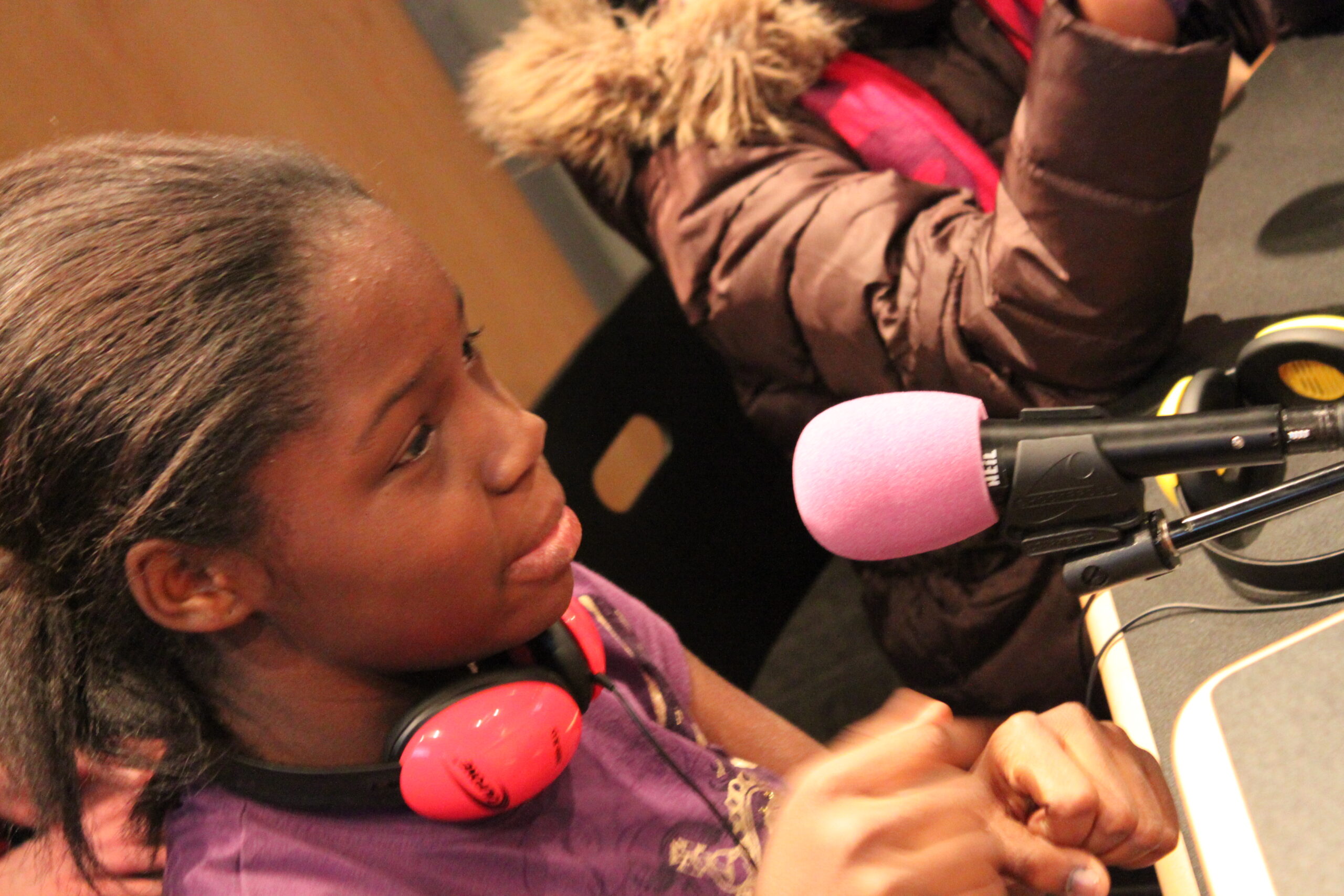 A youth wearing headphones around their neck speaking into a microphone in a radio studio