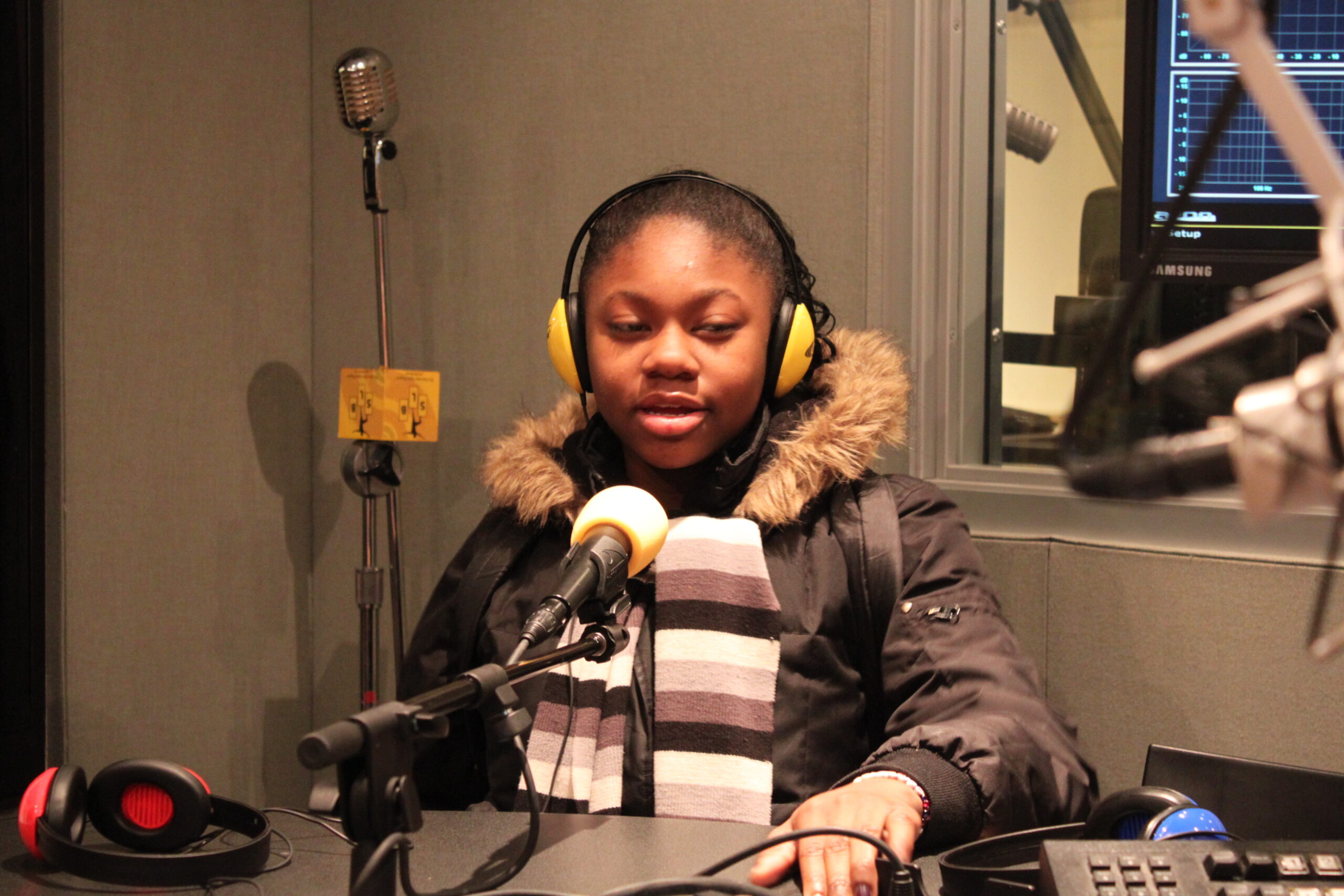 A youth wearing headphones speaking into a microphone in a radio studio