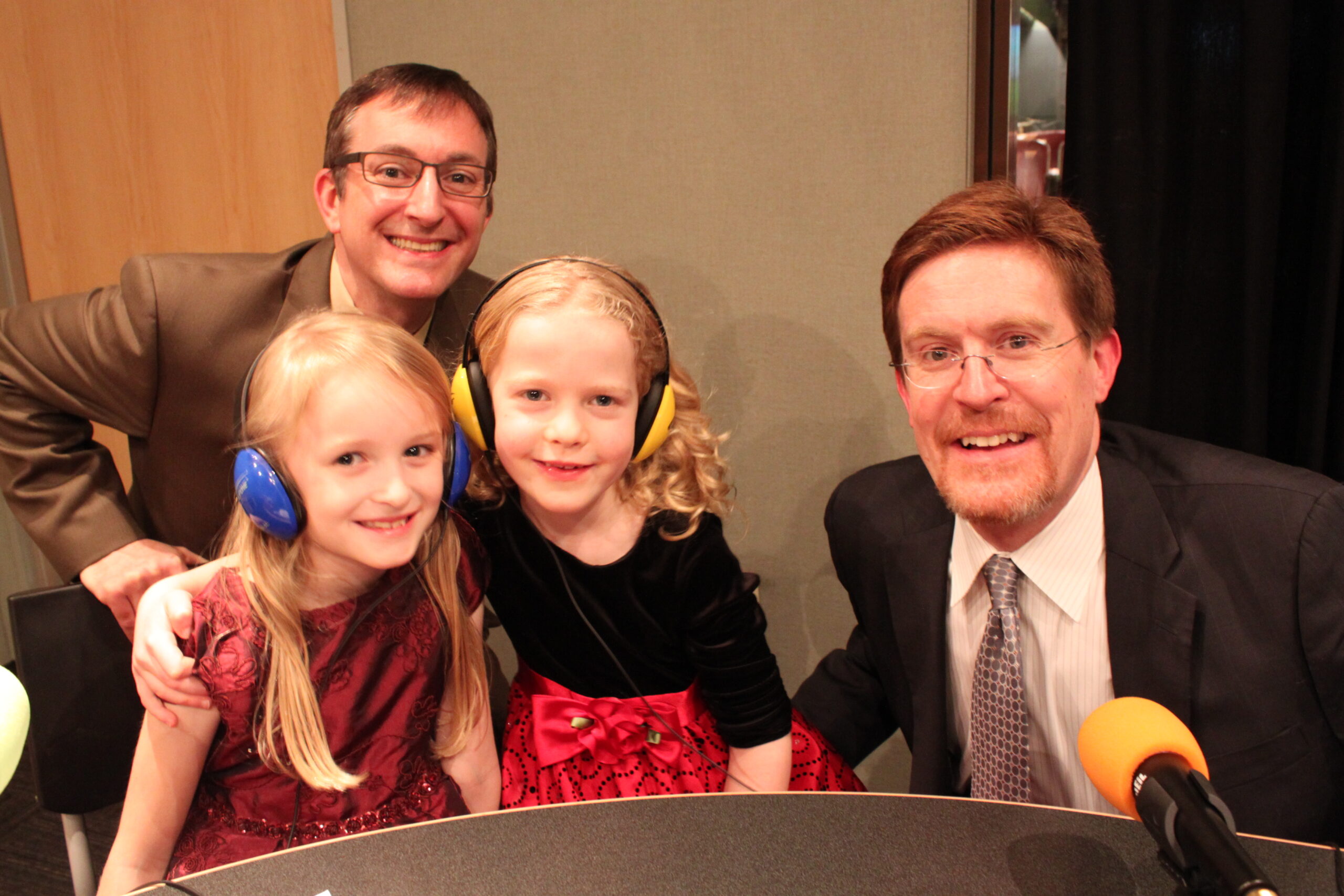 Two youth wearing headphones and two adults, all smiling at the camera in a radio studio