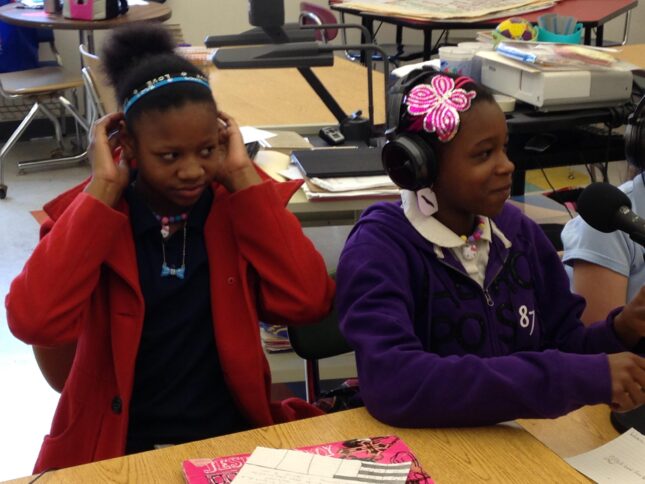 Two youth wearing headphones looking to the right while sitting at classroom desks