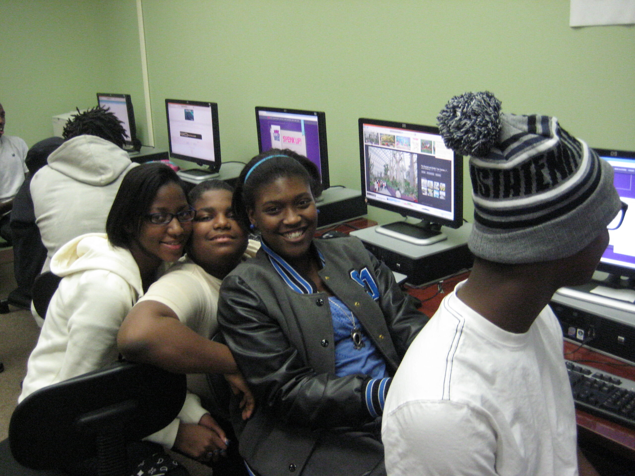 Three youth smiling at the camera while sitting at computers
