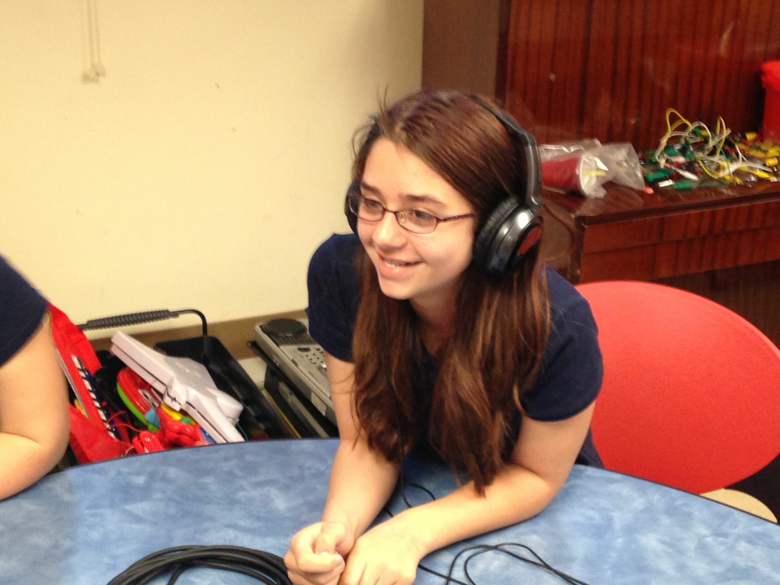 A youth wearing headphones smiling and leaning on a blue table
