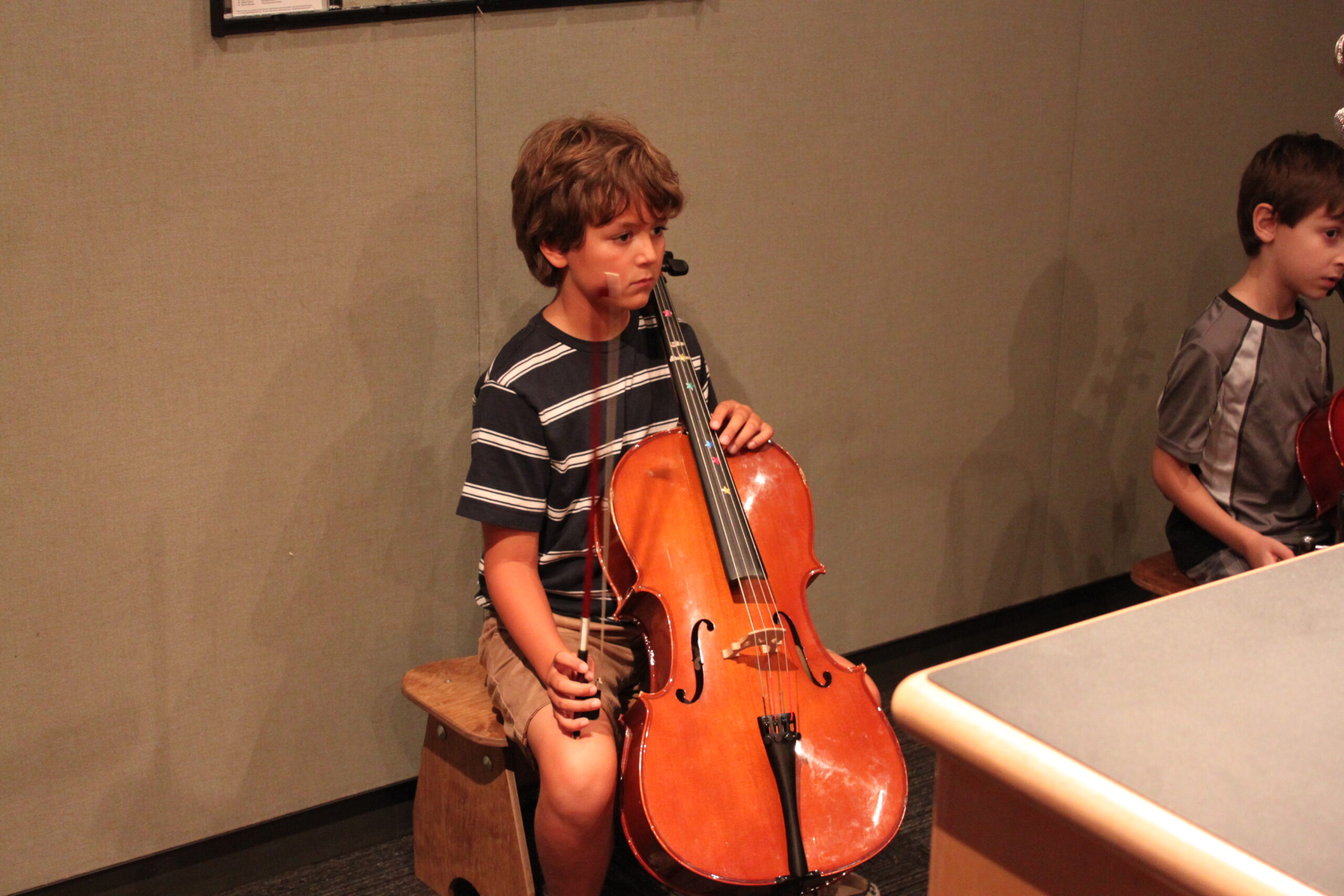 Two youth, one sitting and holding a cello, in a radio studio