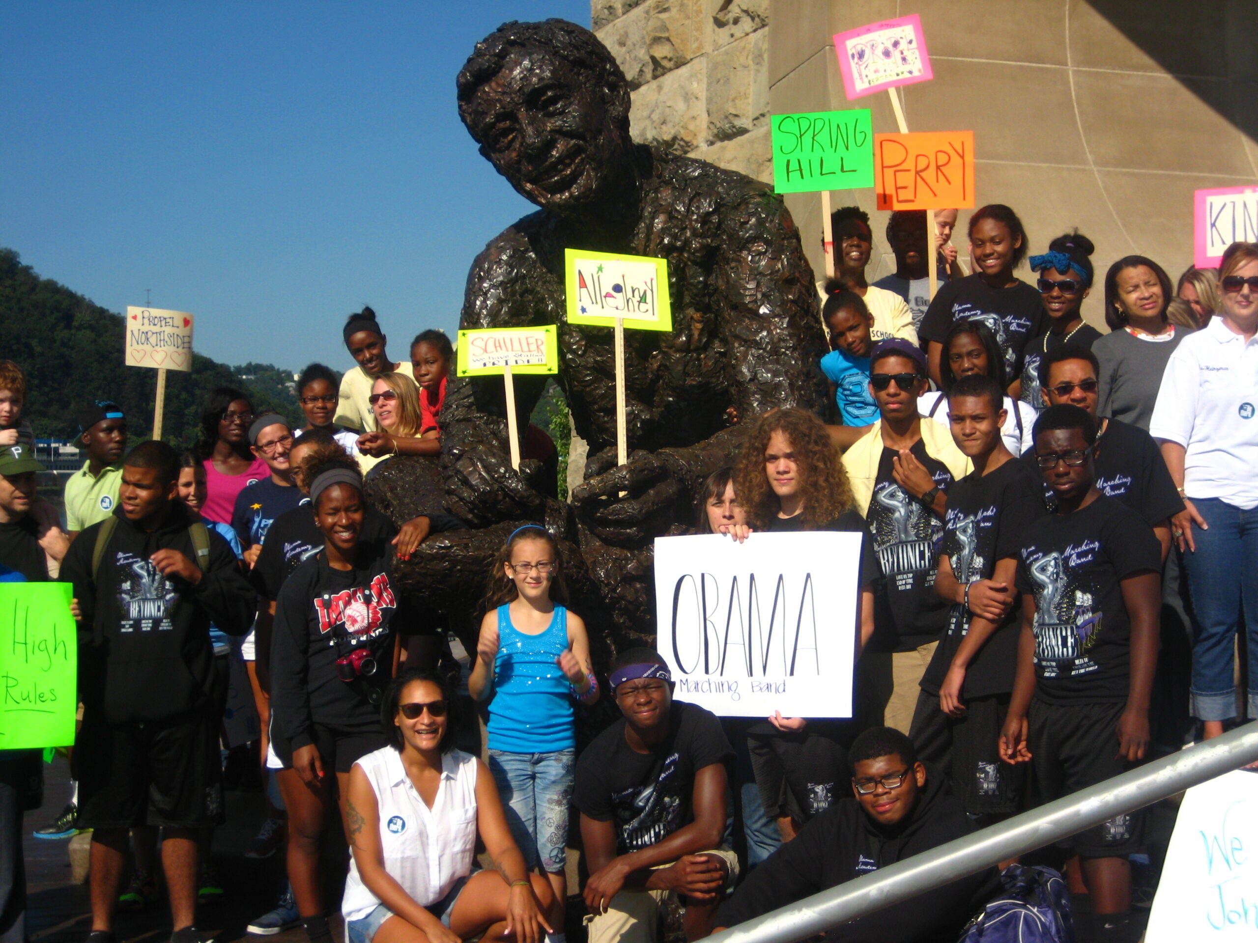 A large group of individuals holding signs while sitting and standing around a large statue of an adult