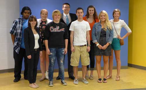 Nine adults smiling and standing in front of a blue wall