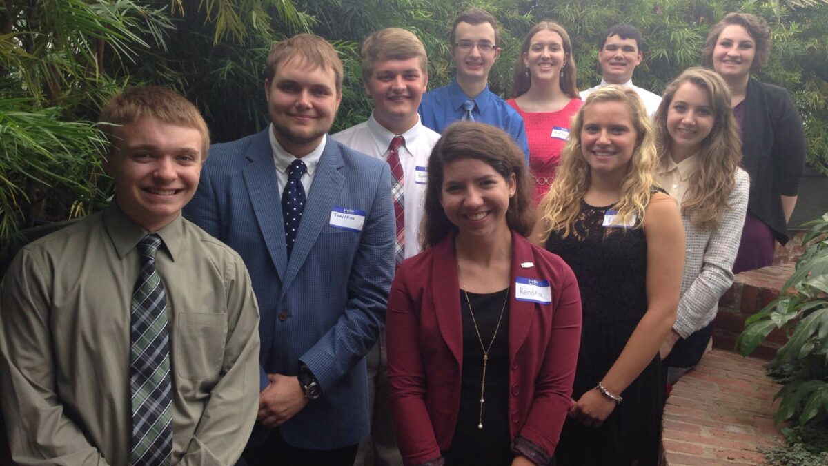 Ten teens smiling and standing in profile in a forest