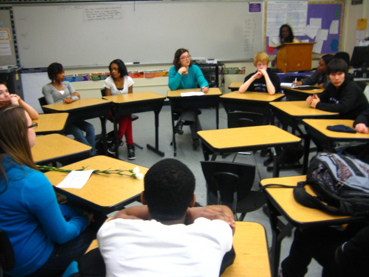 Eight youth sitting at desks in a circle in a classroom in front of a whiteboard