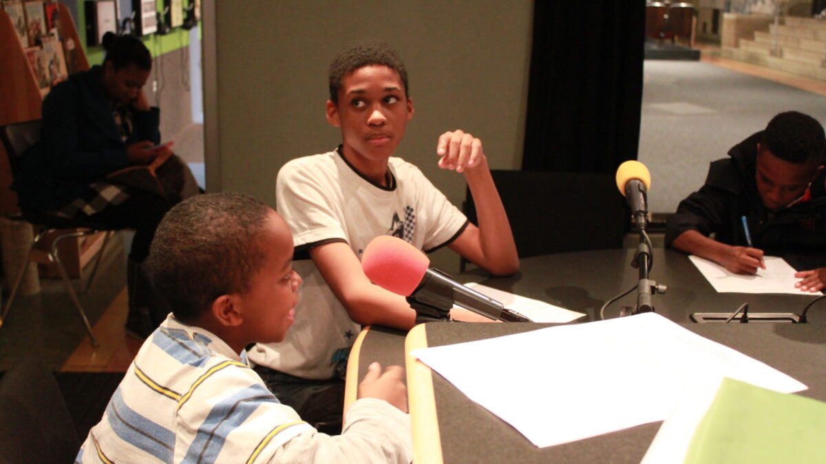 Three youth sitting and speaking into microphones in a radio studio