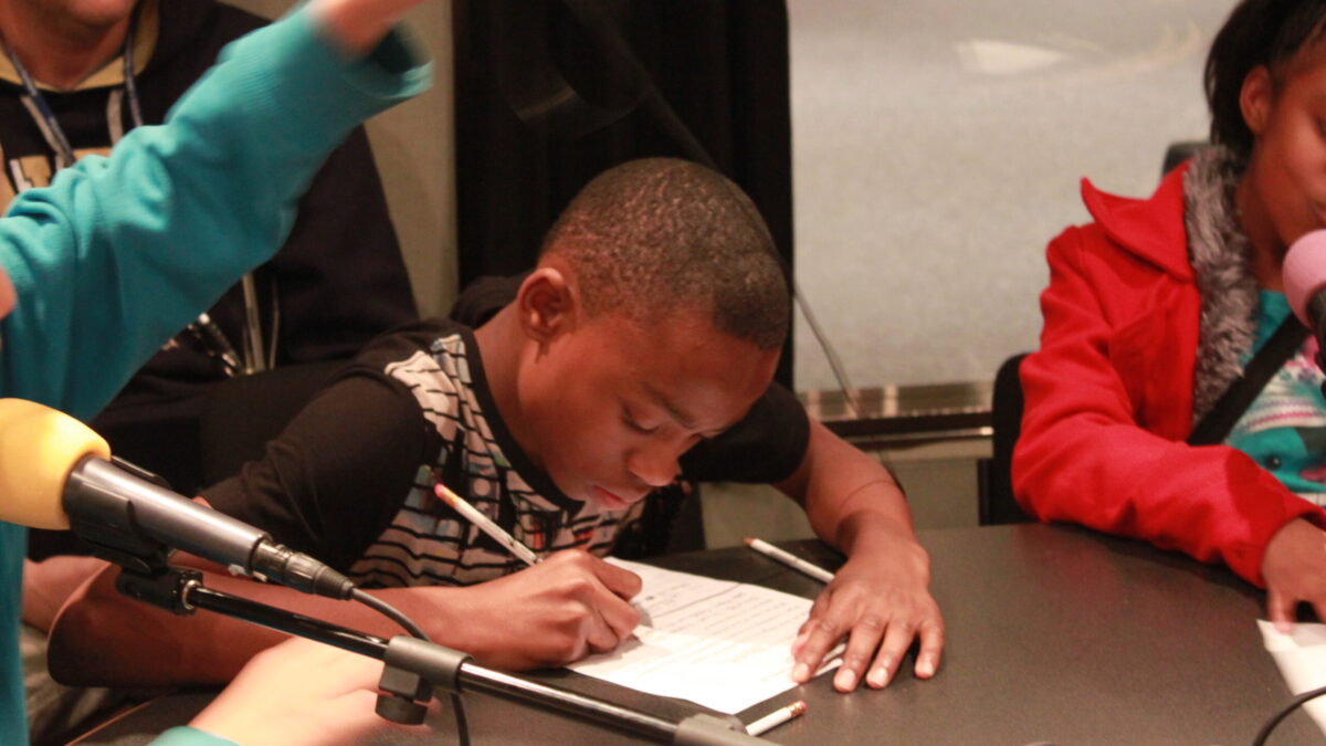 Two youth writing on pieces of paper in a radio studio