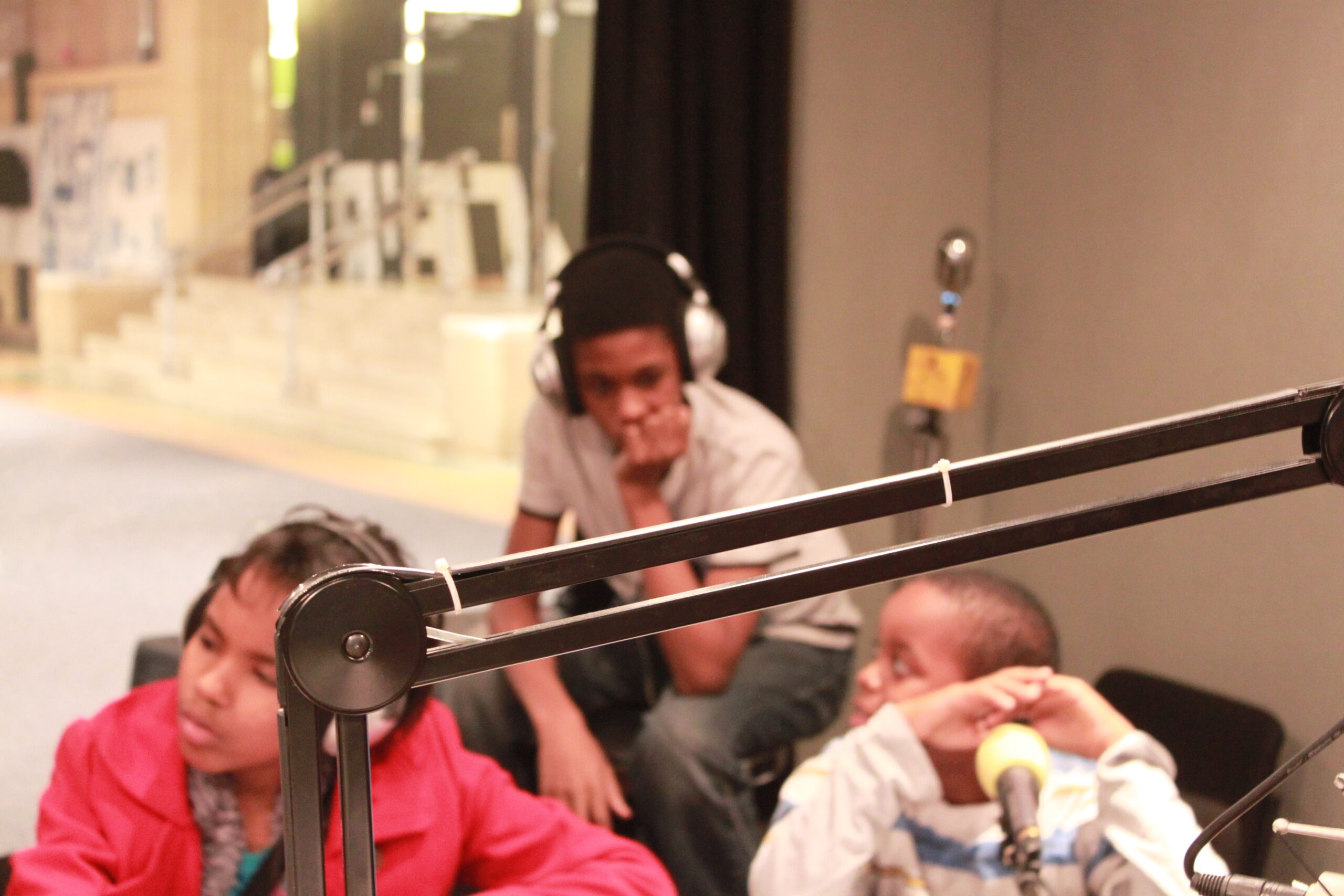 Three youth, two wearing headphones, sitting in a radio studio