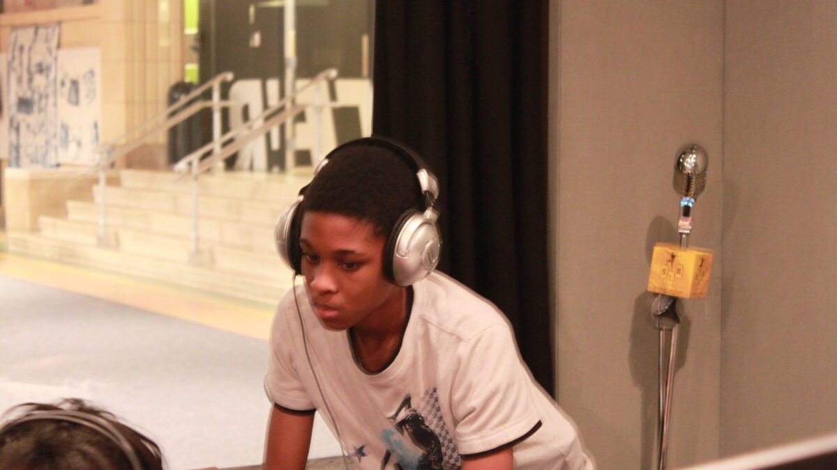 A youth wearing headphones standing hunched over in a radio studio