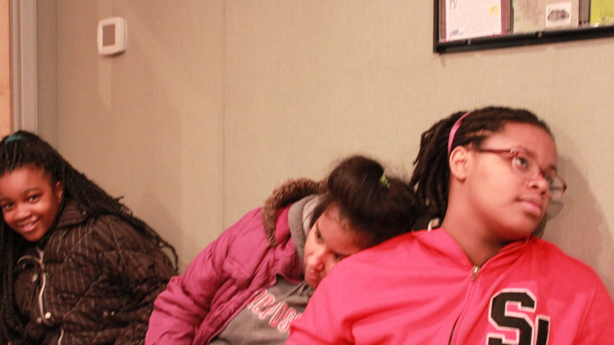 Three youth sitting, one resting their head on another's shoulder, in a radio studio
