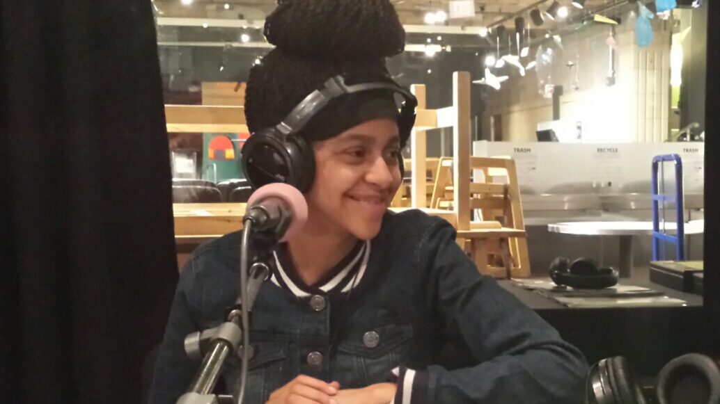 A youth wearing headphones smiling behind a microphone in a radio studio