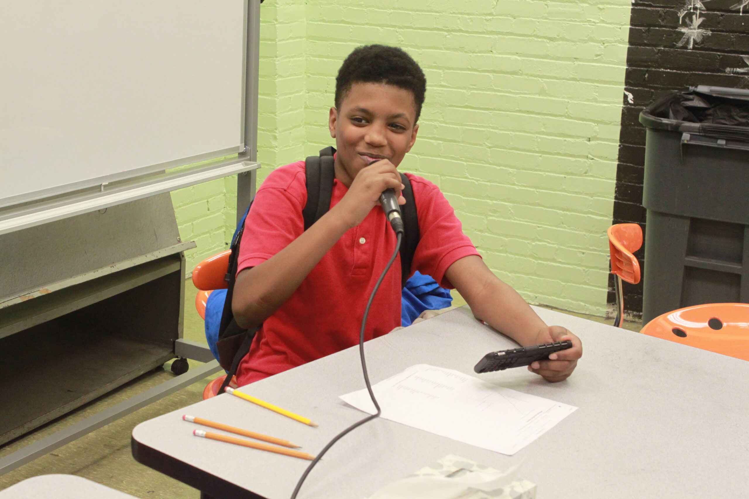 A youth holding and speaking into a microphone sitting in a classroom