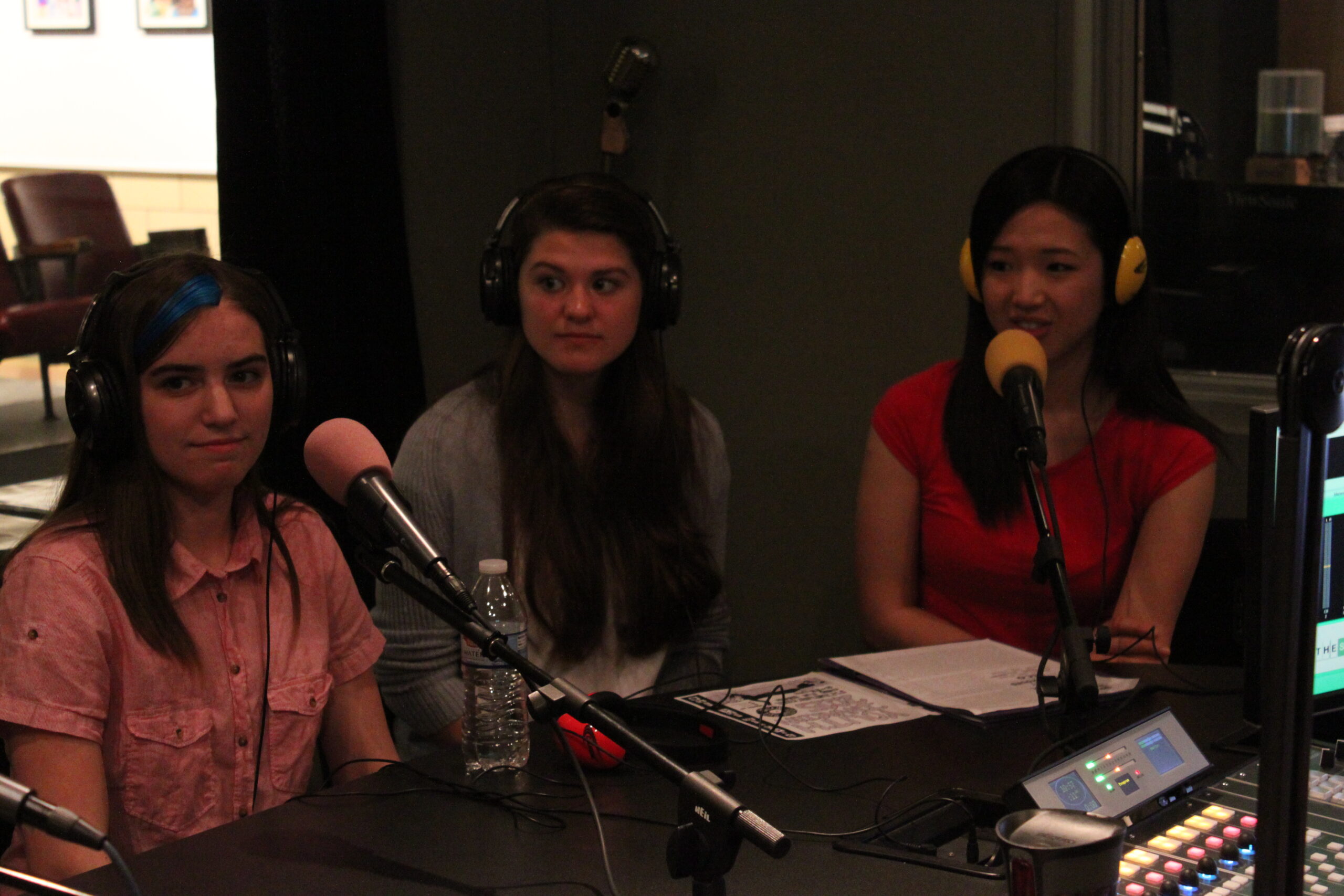 Three teens wearing headphones speaking into microphones in a radio studio
