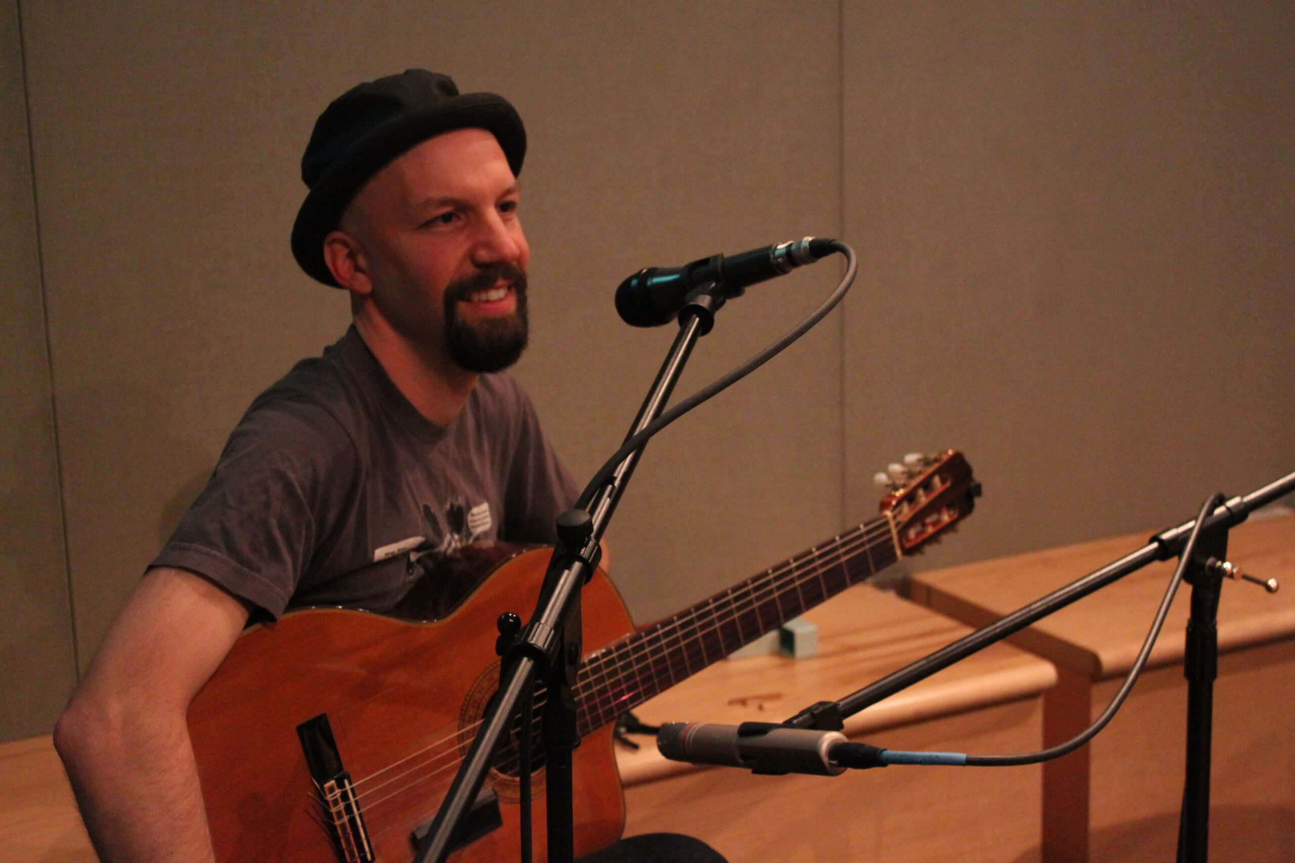 An adult speaking into a microphone and holding an acoustic guitar in a radio studio