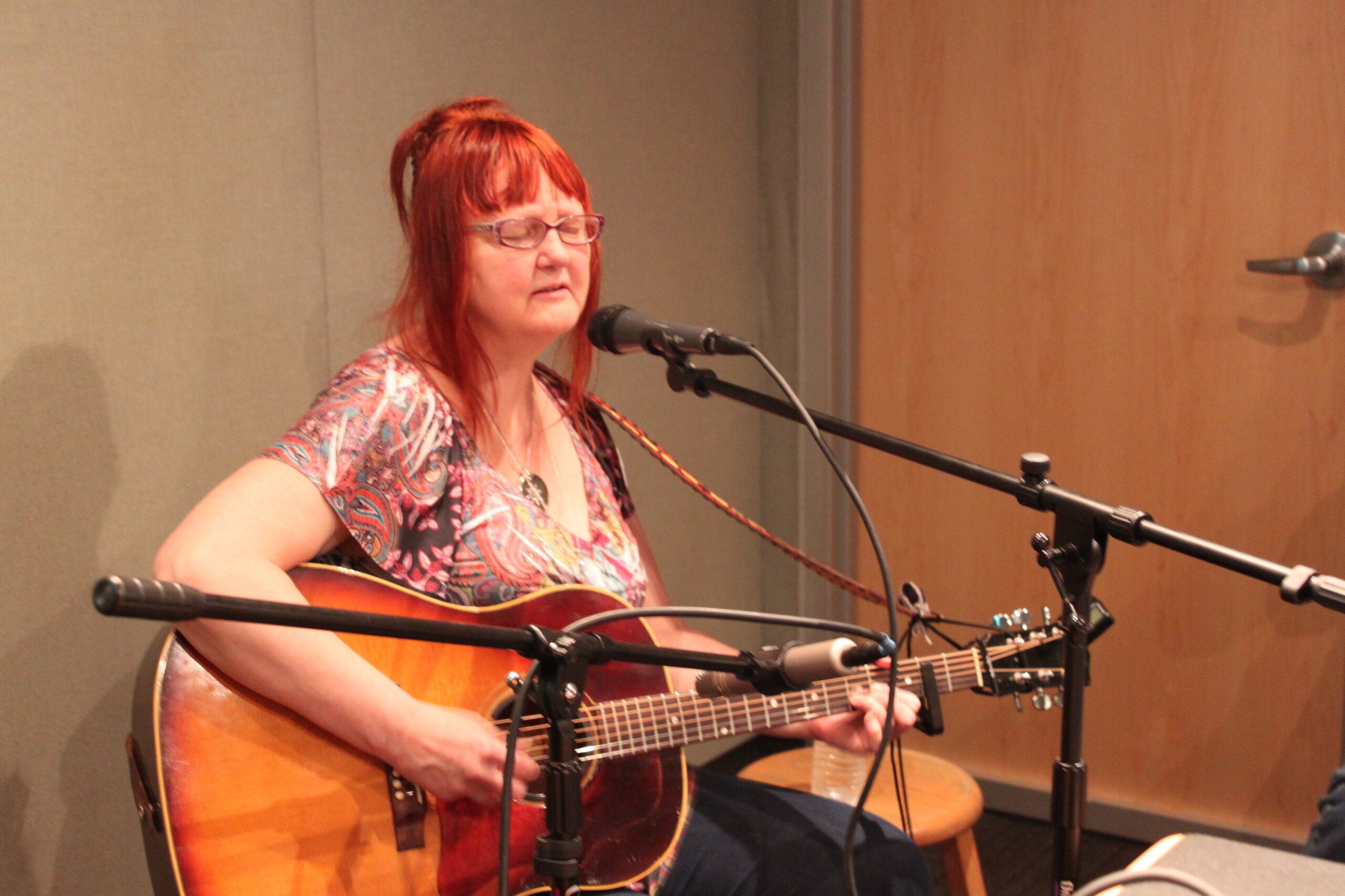 An adult playing an acoustic guitar and singing into a microphone in a radio studio