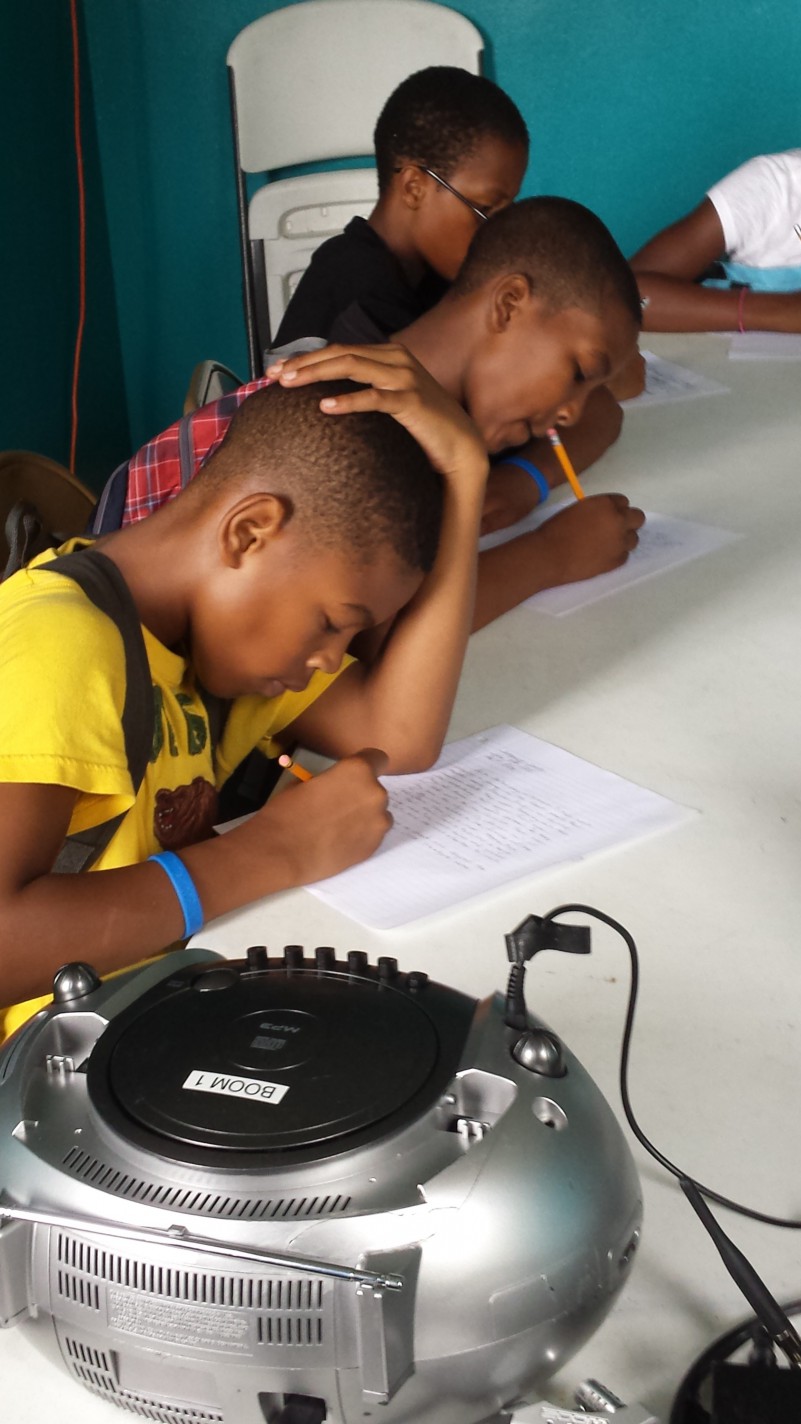 Three youth looking down and writing on pieces of paper in a blue room