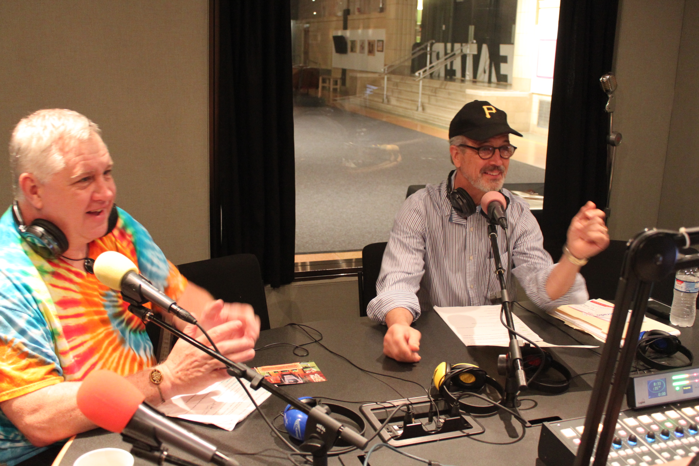 Two adults wearing headphones speaking into microphones in a radio studio