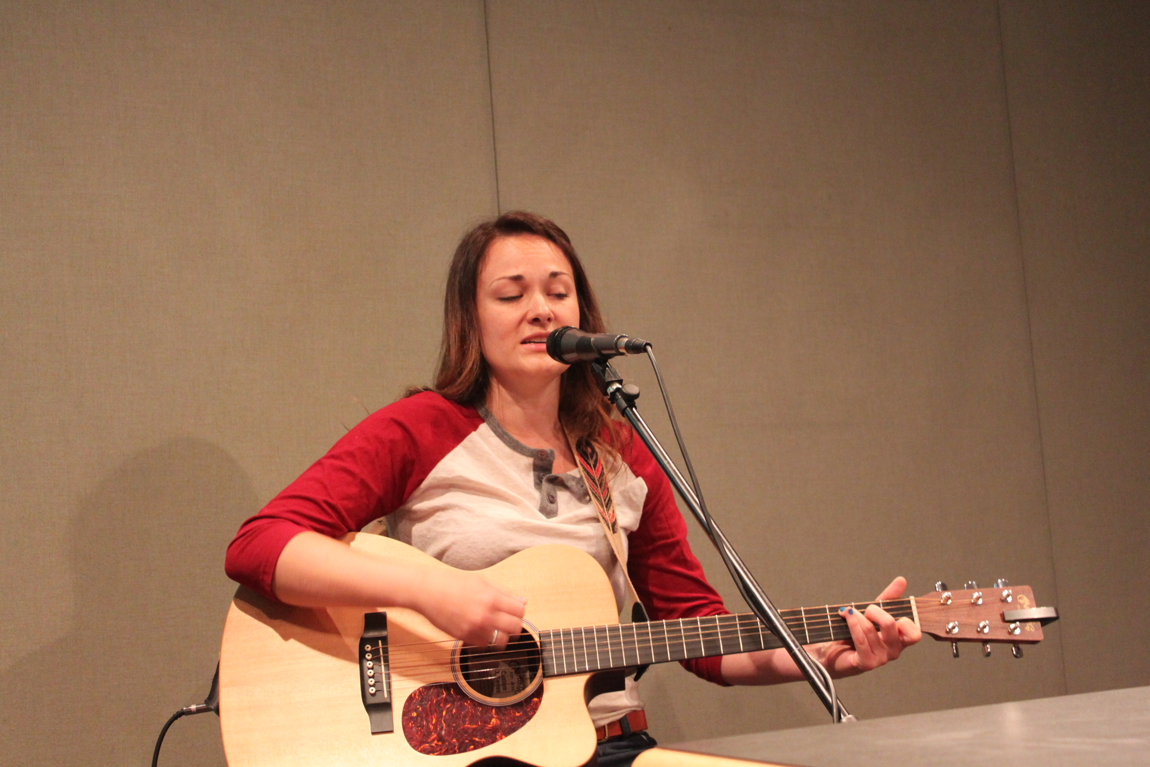 An adult playing an acoustic guitar and singing into a microphone in a radio studio