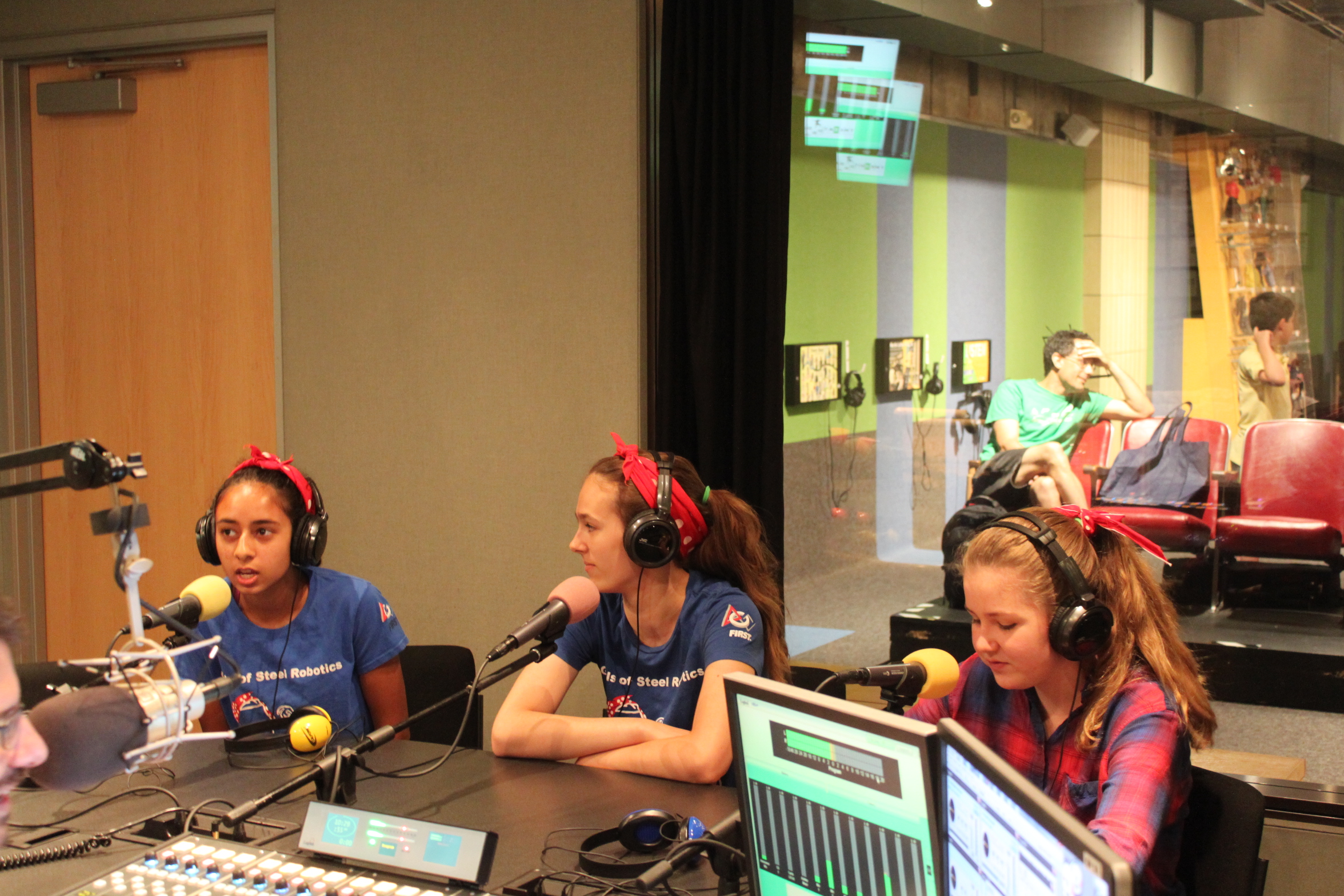 Three teens wearing headphones speaking into microphones in a radio studio