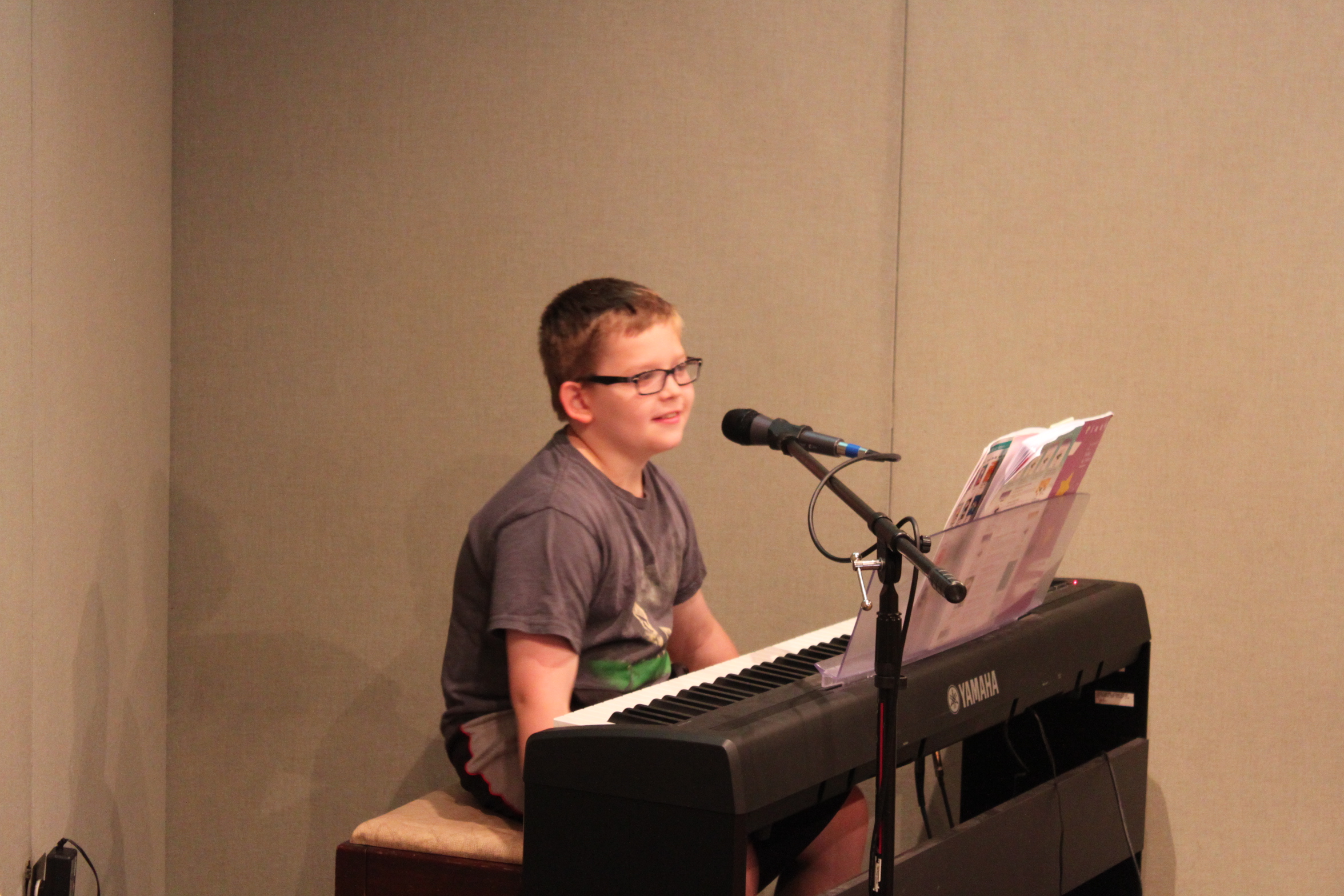 A youth sitting behind a piano keyboard and a microphone in a radio studio