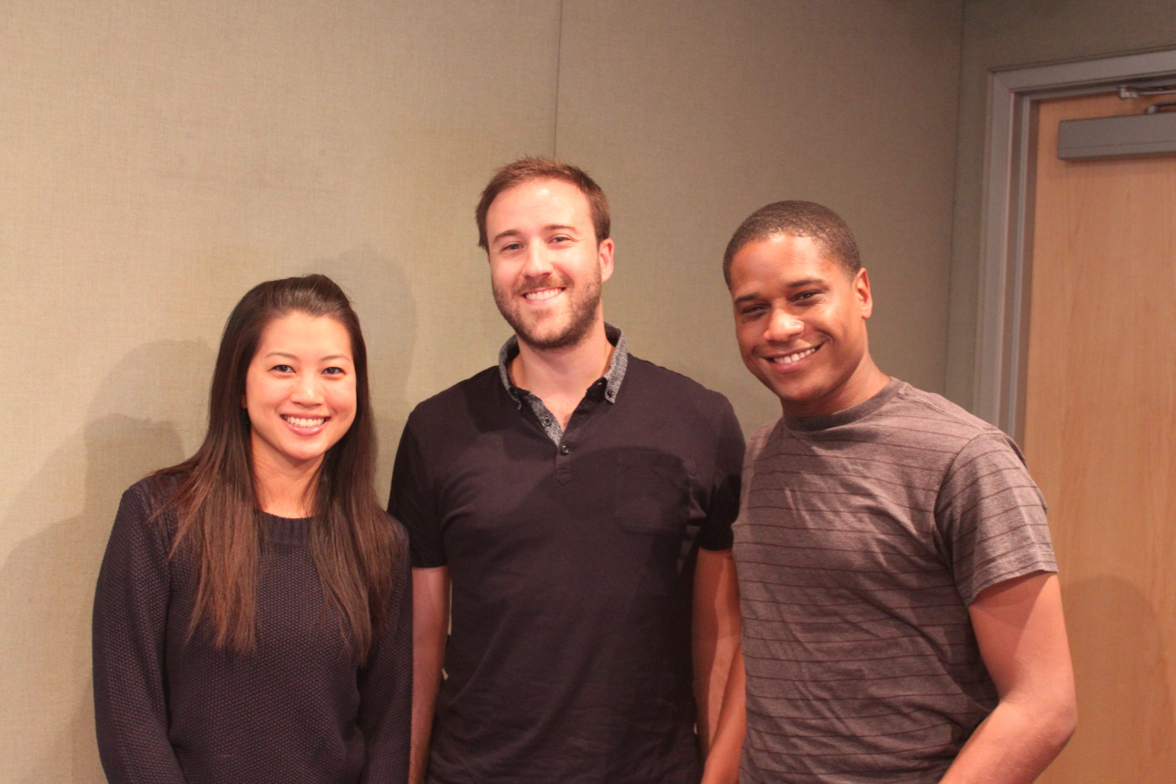 Three adults smiling and posing in profile in a radio studio
