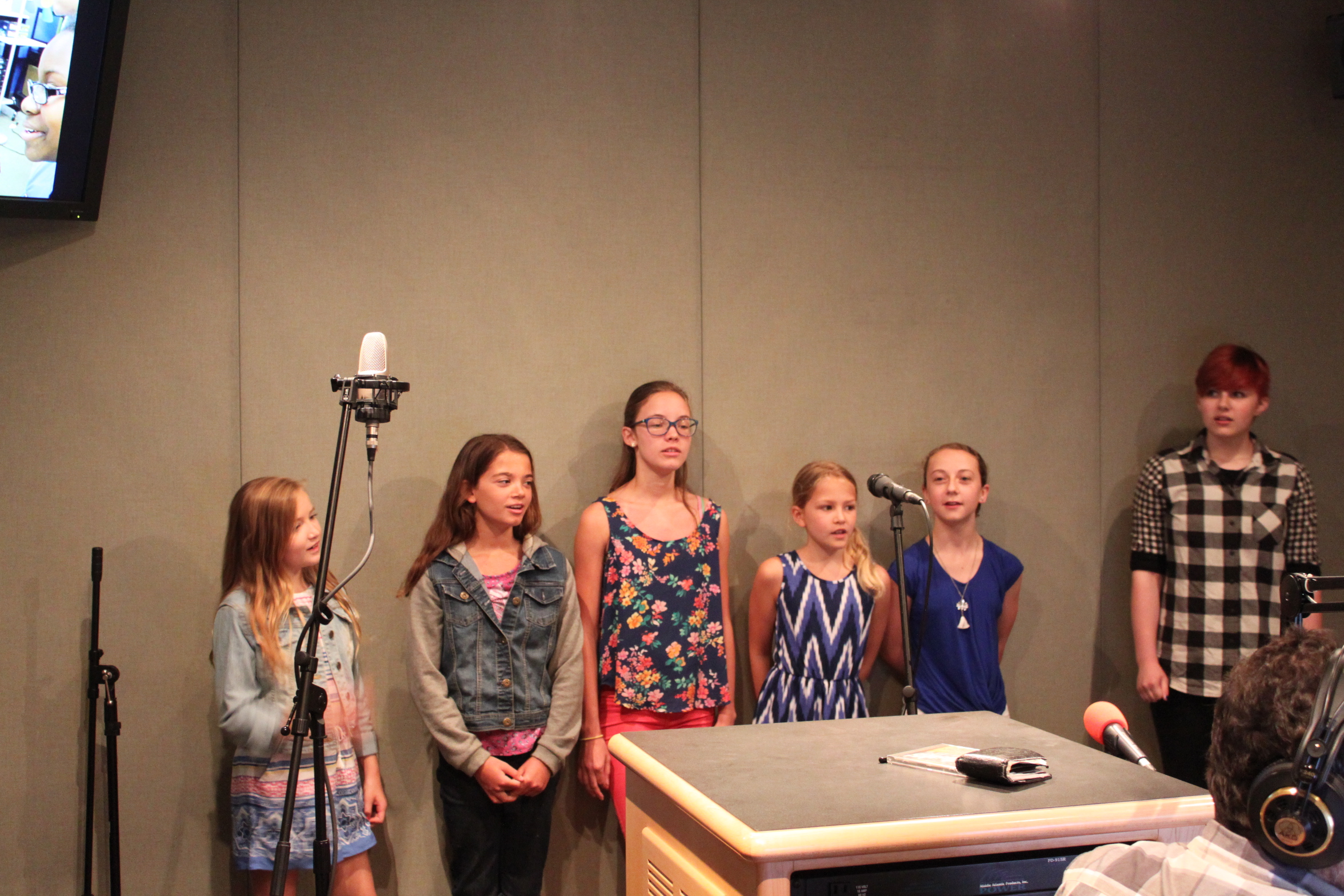 Six youth standing behind a microphone in a radio studio