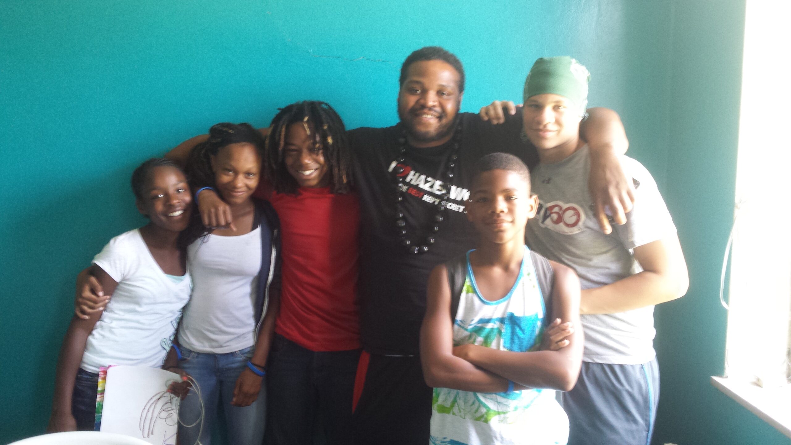 Four youth and two adults smiling and posing in a blue room