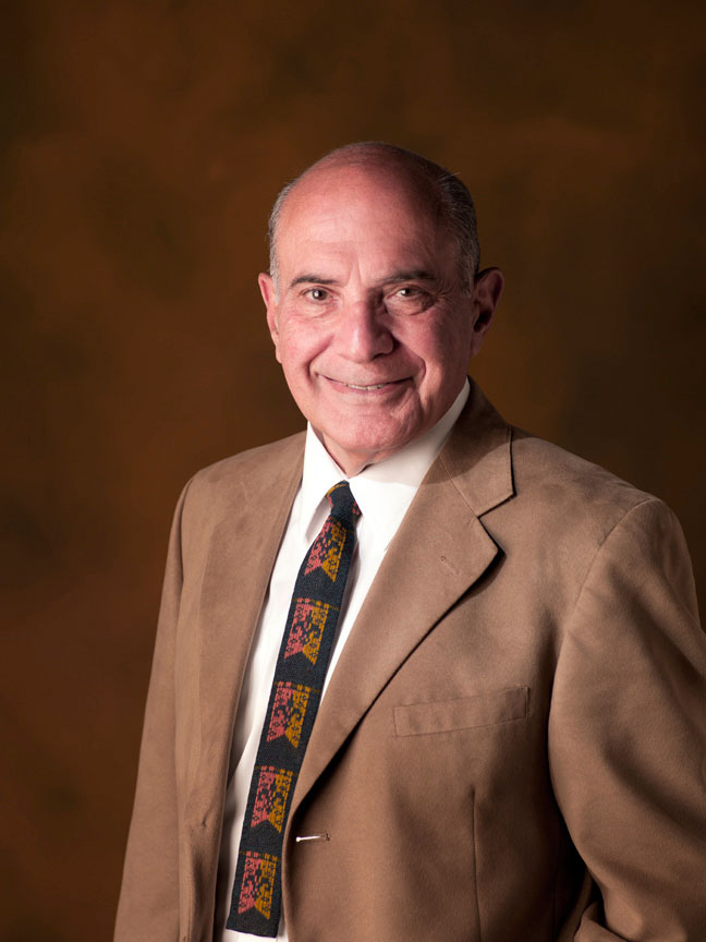 An adult wearing a brown suit smiling and posing in profile