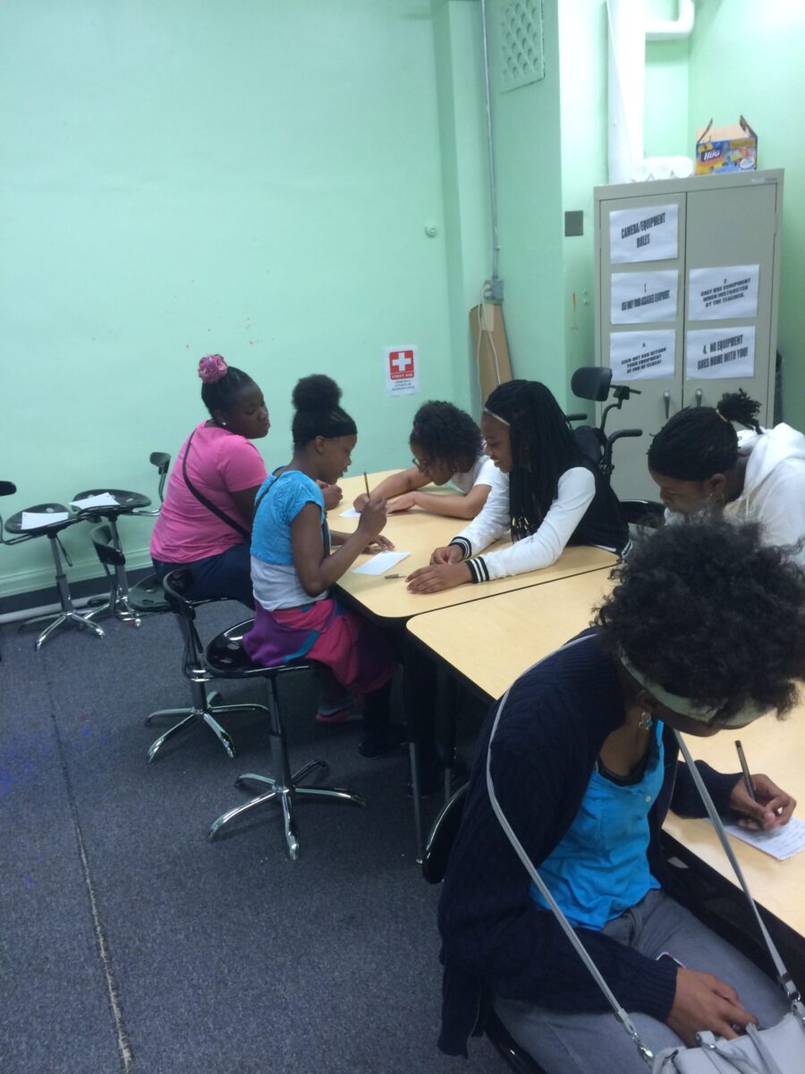 Six youth writing on pieces of paper on classroom desks
