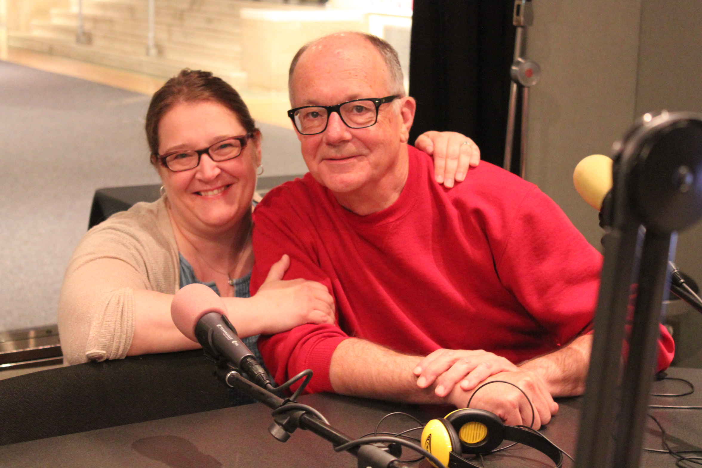 Two adults sitting behind a microphone in a radio studio