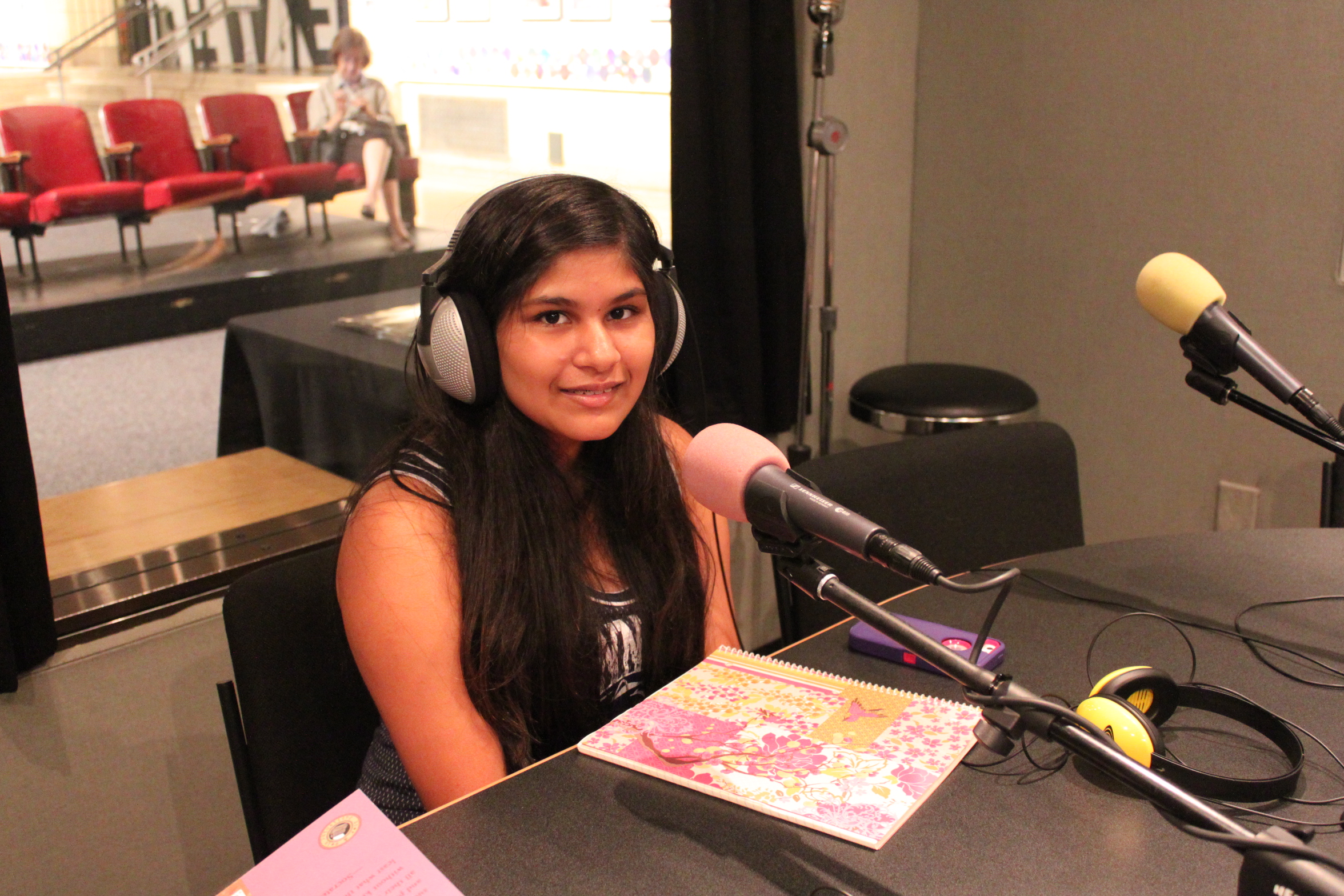 A youth wearing headphones smiling and sitting behind a microphone in a radio studio