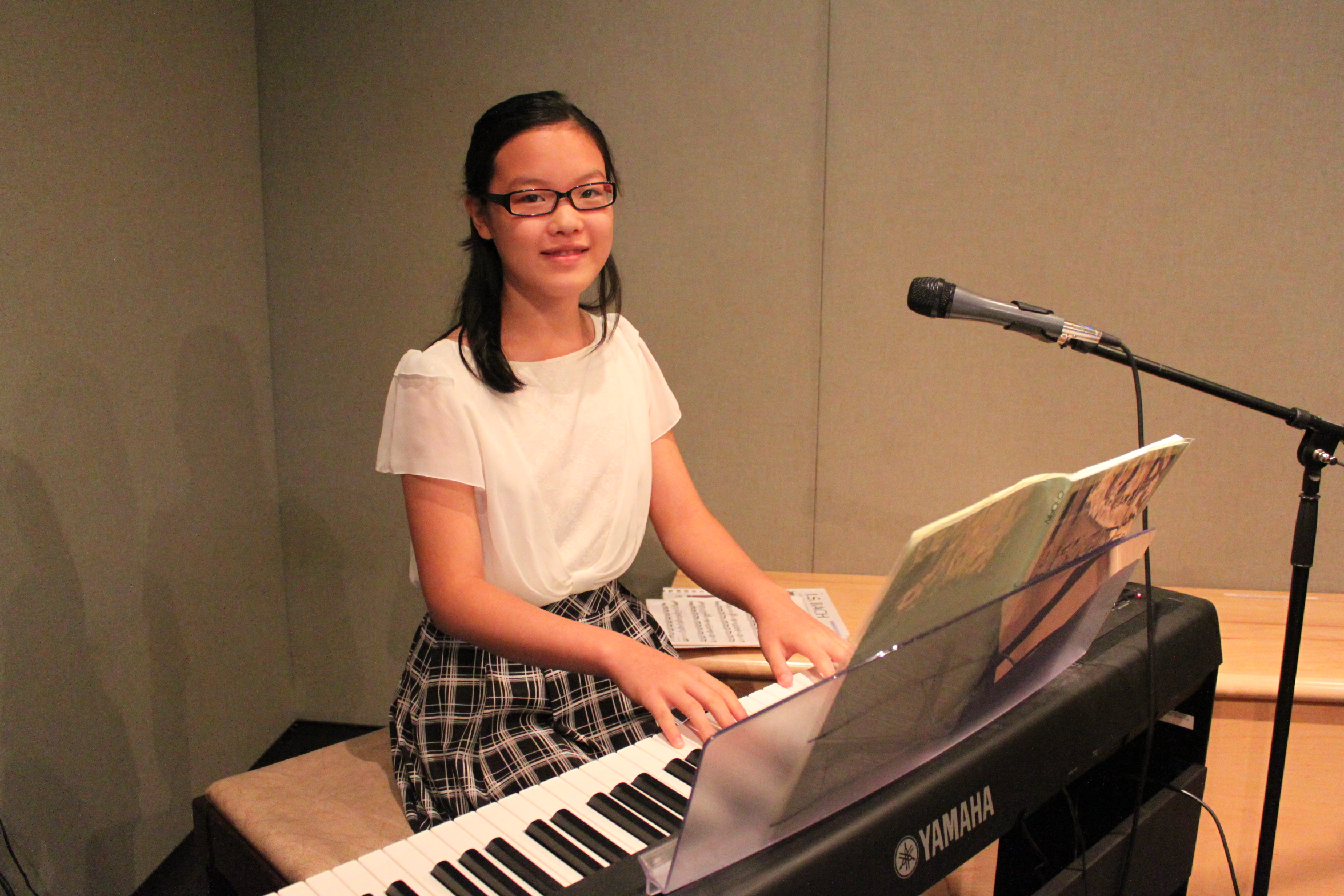 A youth smiling while sitting at a piano keyboard behind a microphone in a radio studio