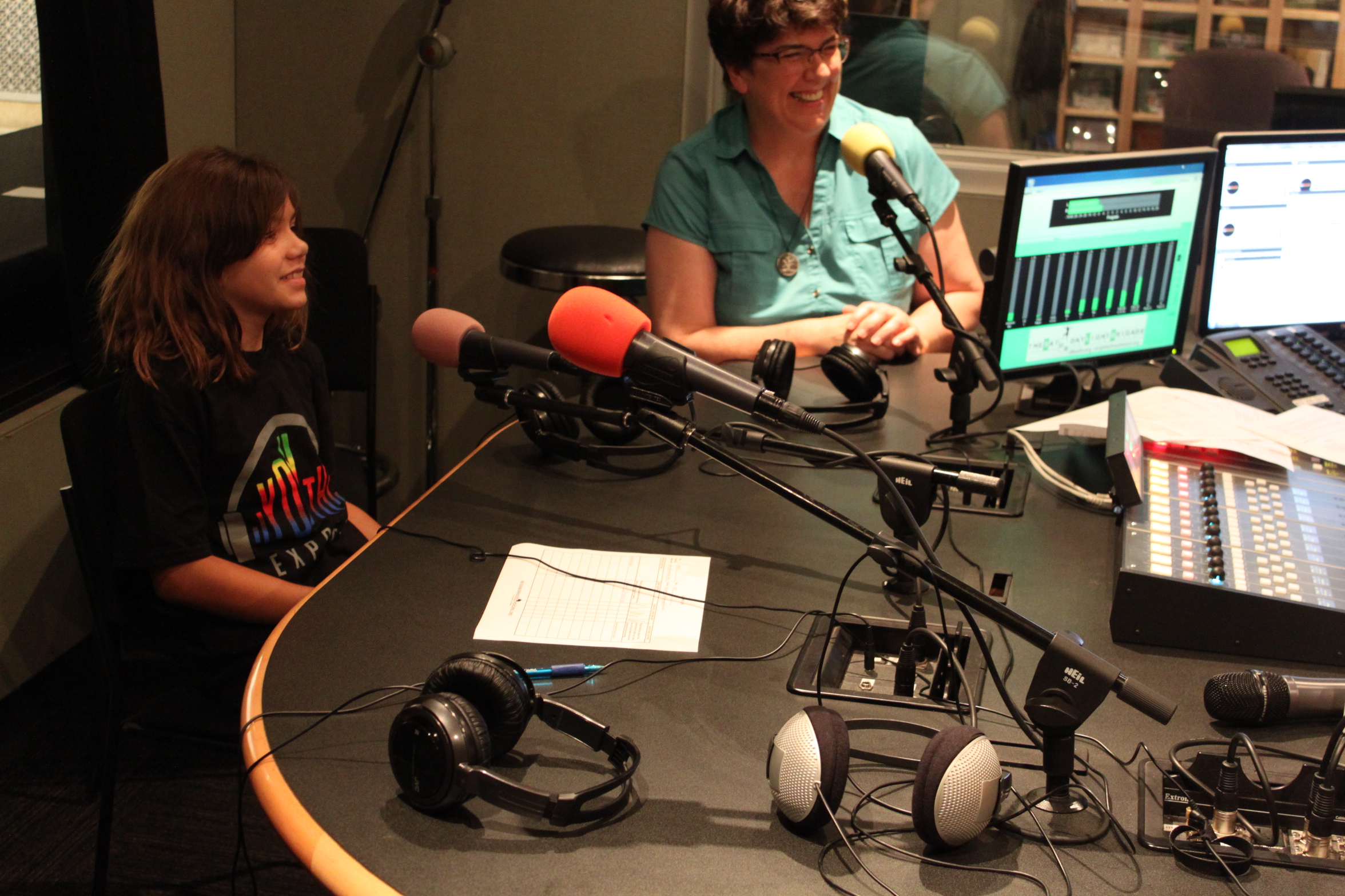A youth and an adult sitting behind microphones being interviewed in a radio studio