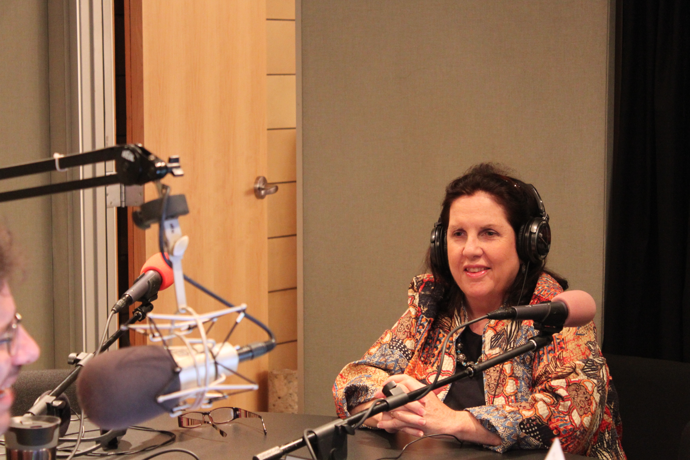 An adult wearing headphones speaking into a microphone being interviewed in a radio studio