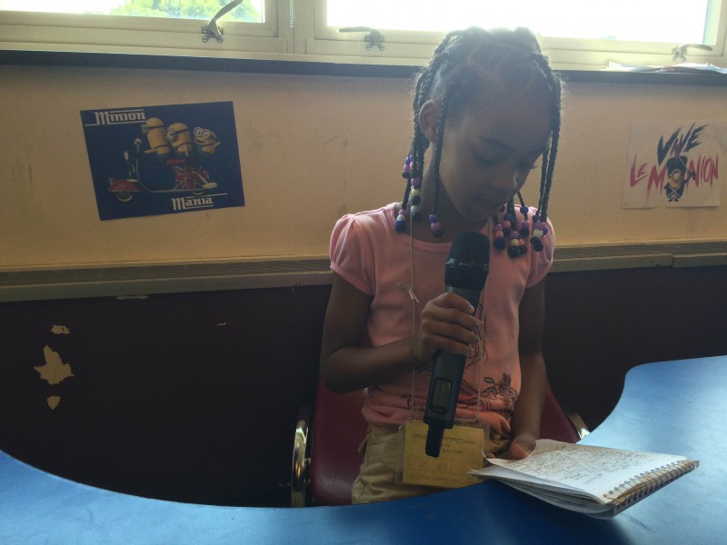 A youth reading from a piece of paper into a microphone in a classroom