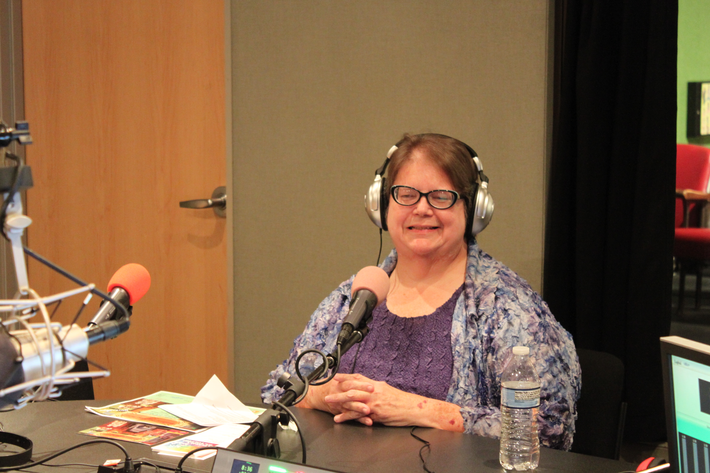 An adult wearing headphones sitting behind a microphone in a radio studio
