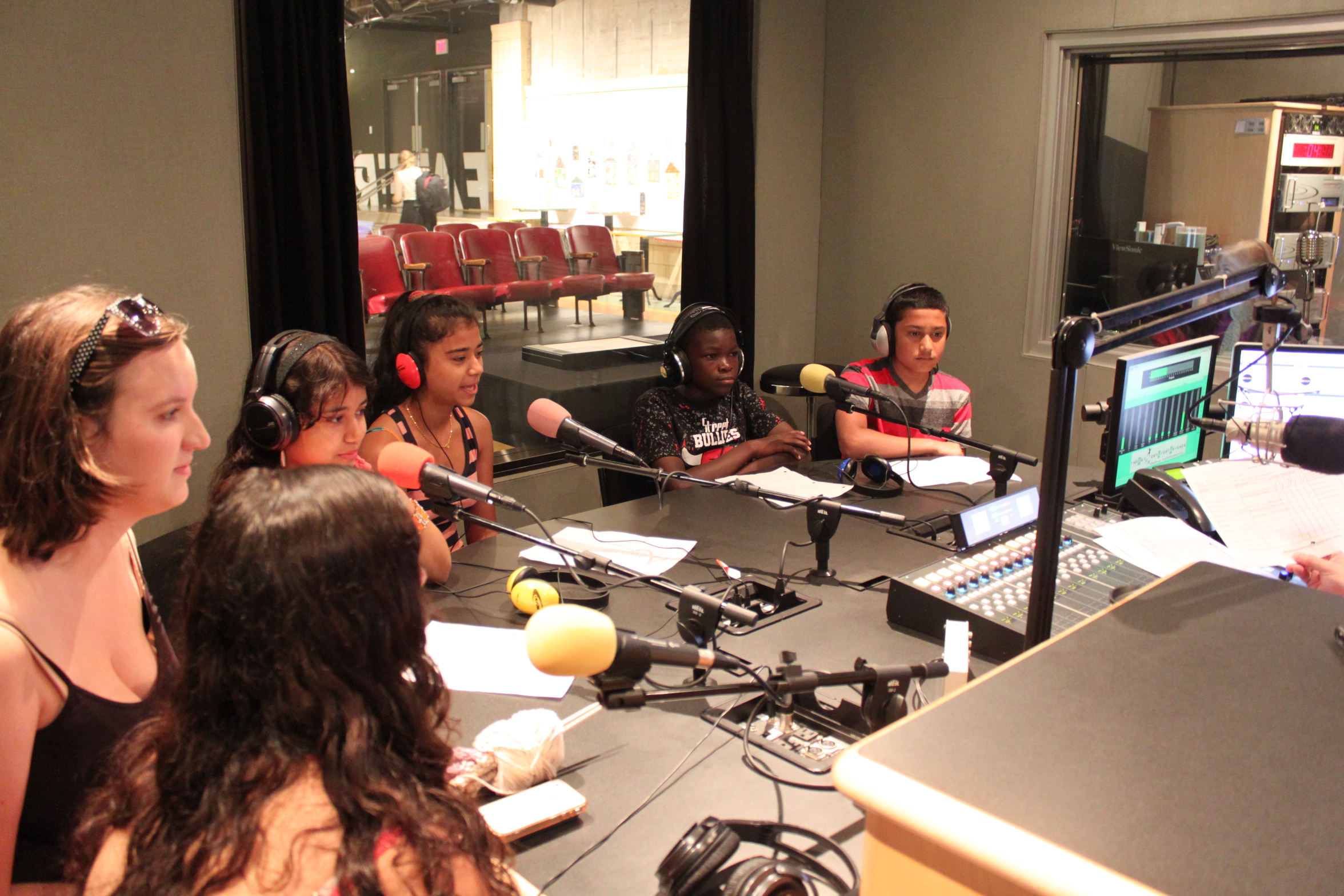 Six youth wearing headphones speaking into microphones in a radio studio