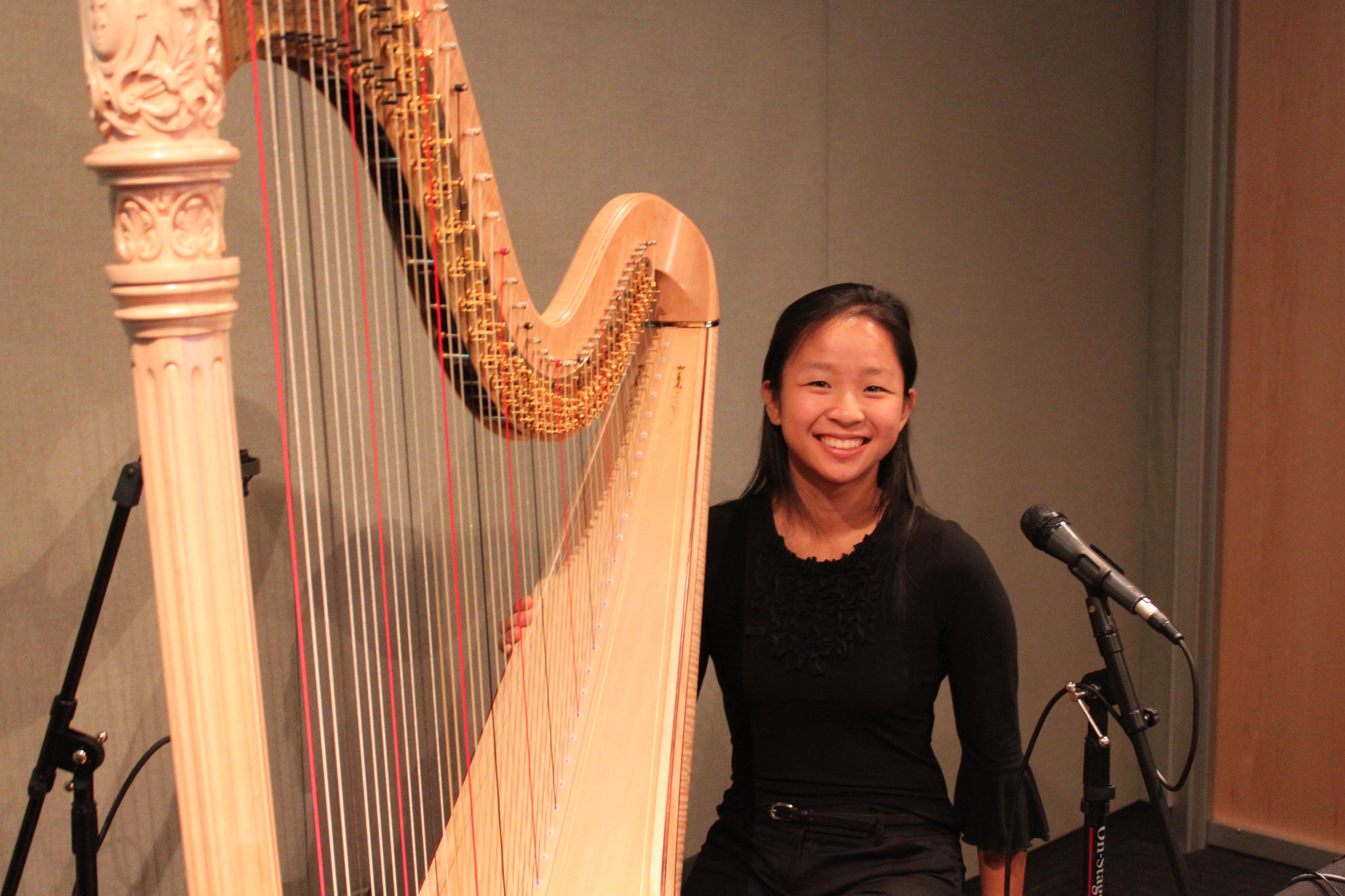 A teen sitting behind a harp smiling in a radio studio