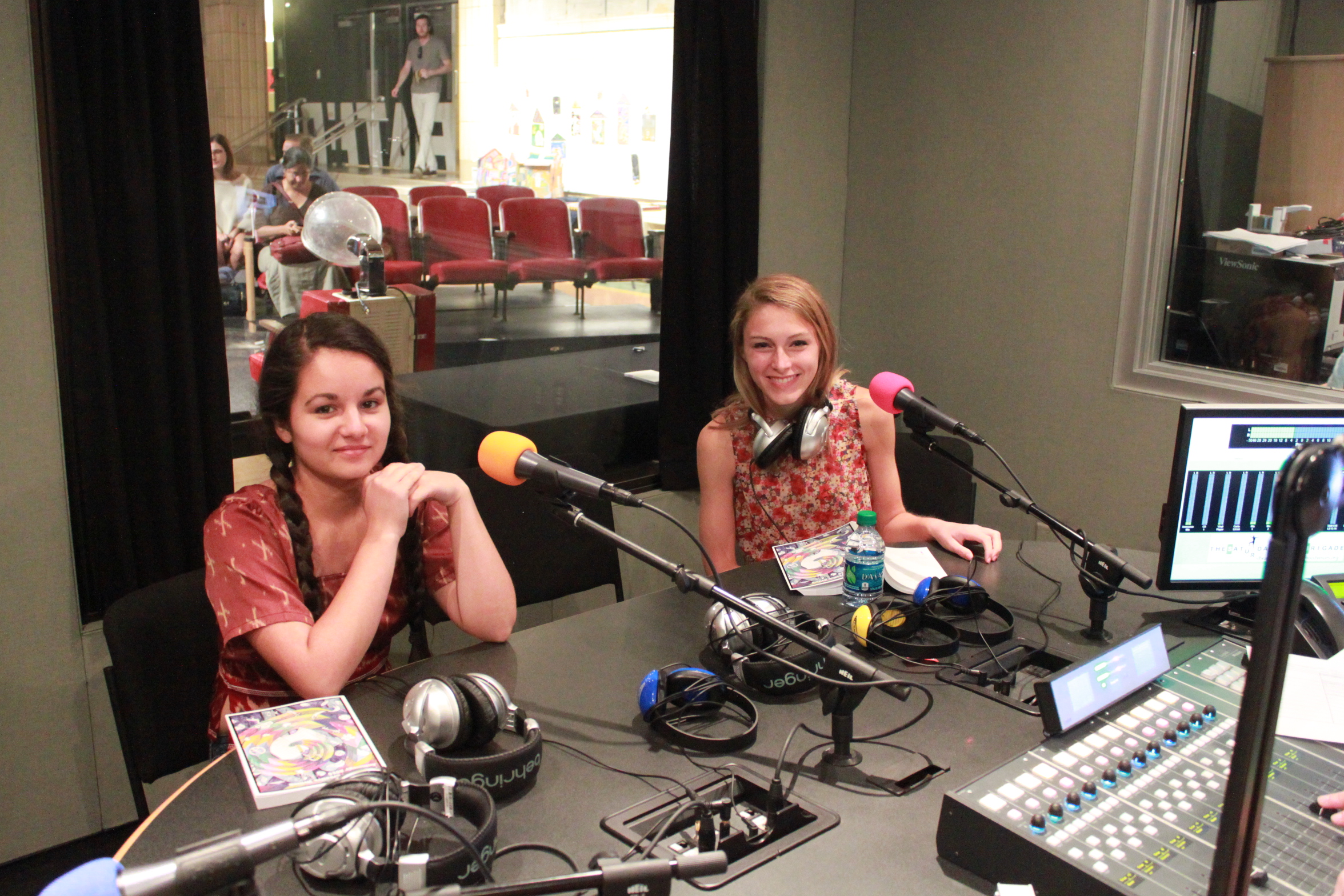Two teens sitting behind microphones in a radio studio