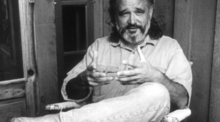 A black and white image of an adult sitting on a chair on a porch