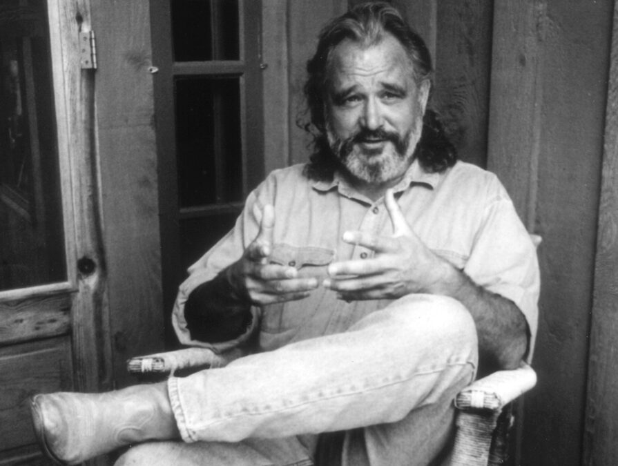 A black and white image of an adult sitting on a chair on a porch