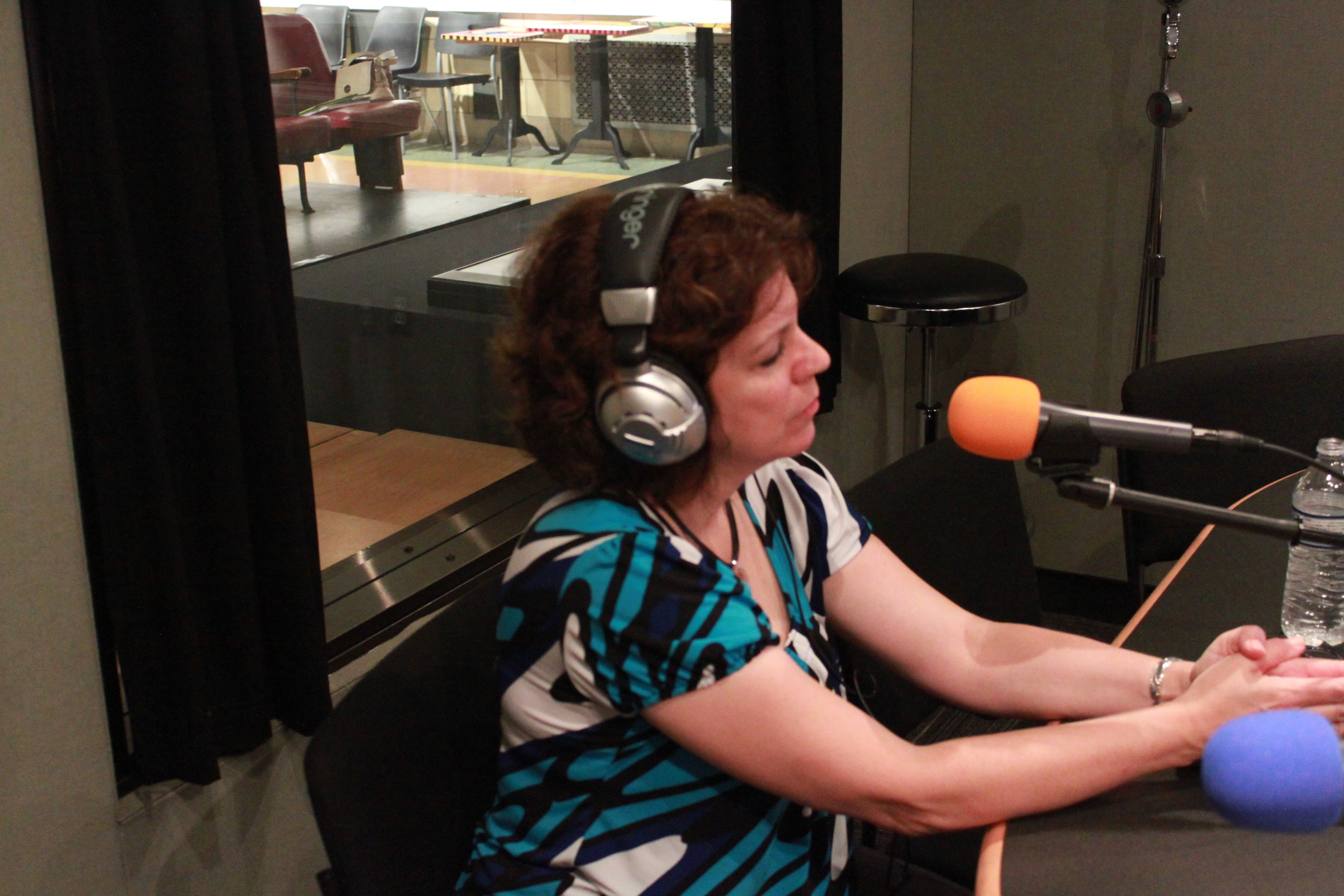 An adult wearing headphones speaking into a microphone in a radio studio
