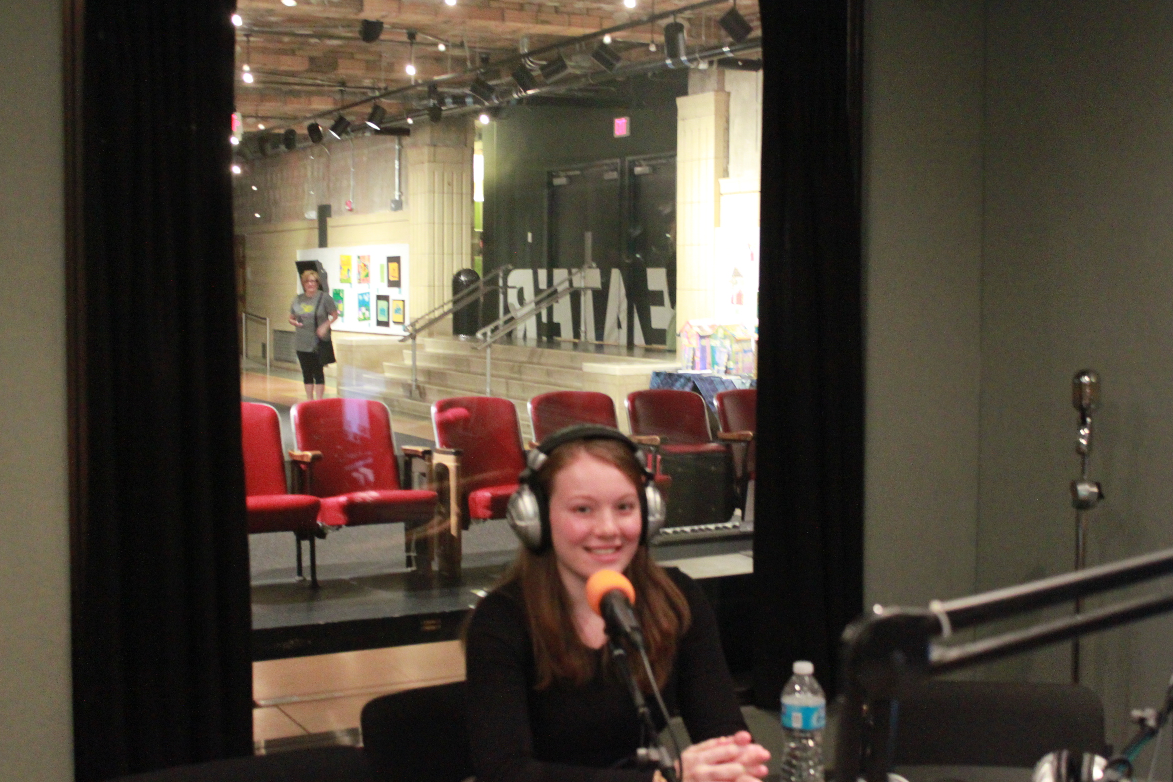 A teen wearing headphones smiling while sitting behind a microphone in a radio studio