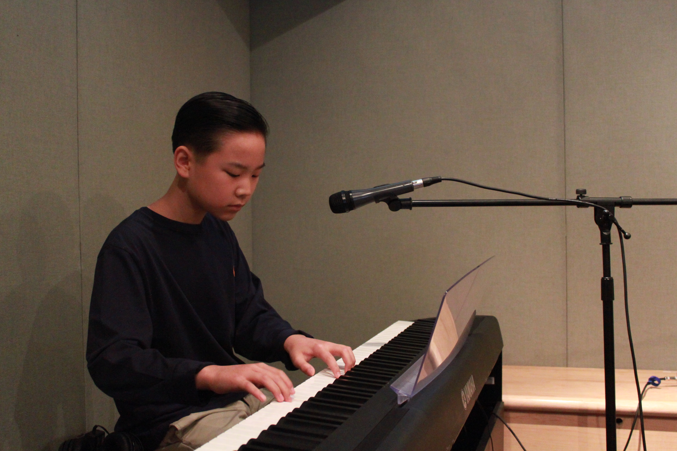 A youth playing a piano keyboard sitting behind a microphone in a radio studio