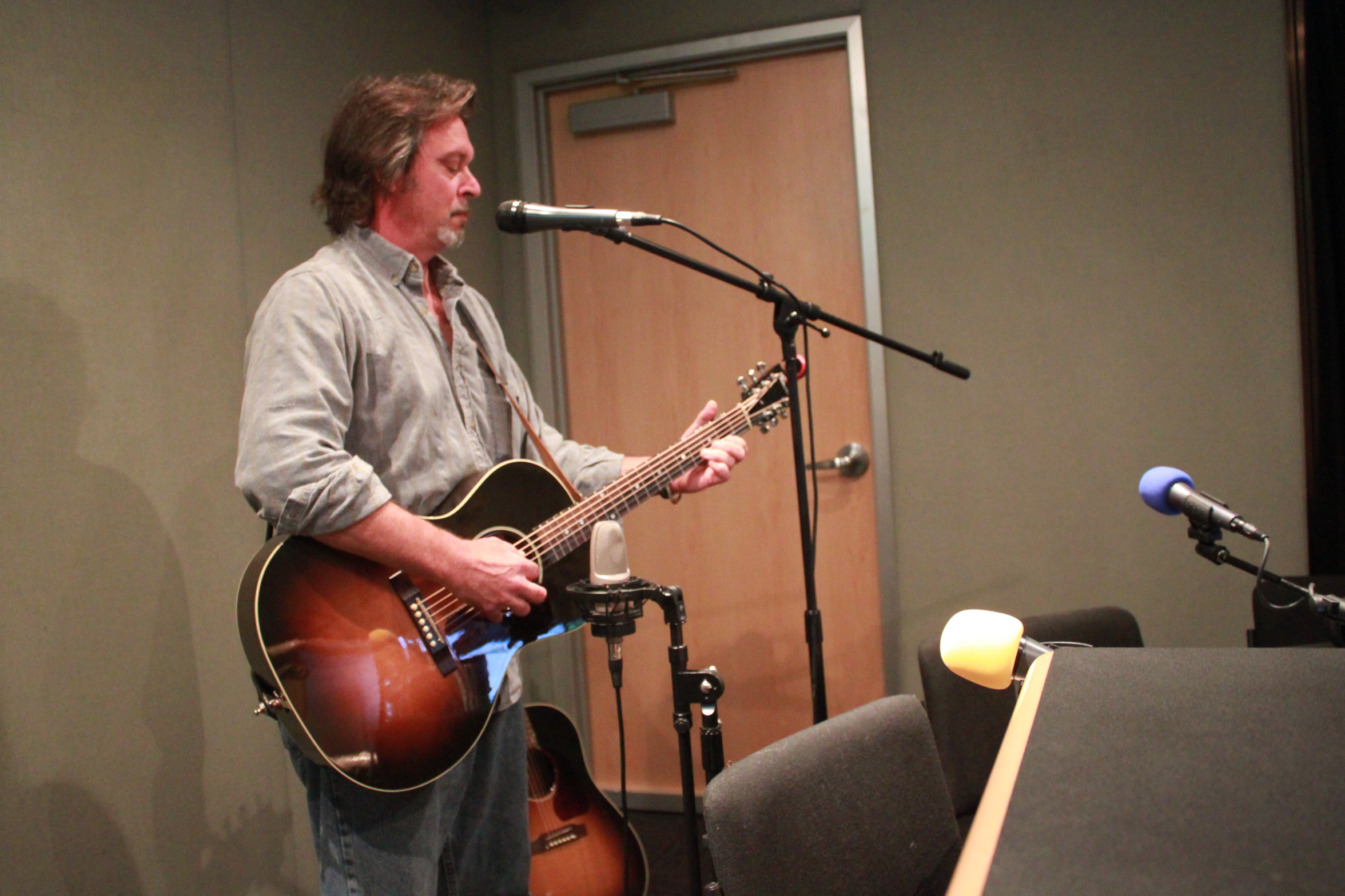An adult playing an acoustic guitar and singing into a microphone in a radio studio