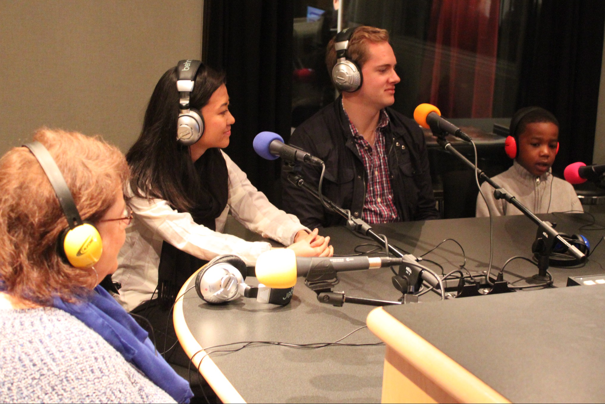 Three adults and one youth wearing headphones speaking into microphones in a radio studio